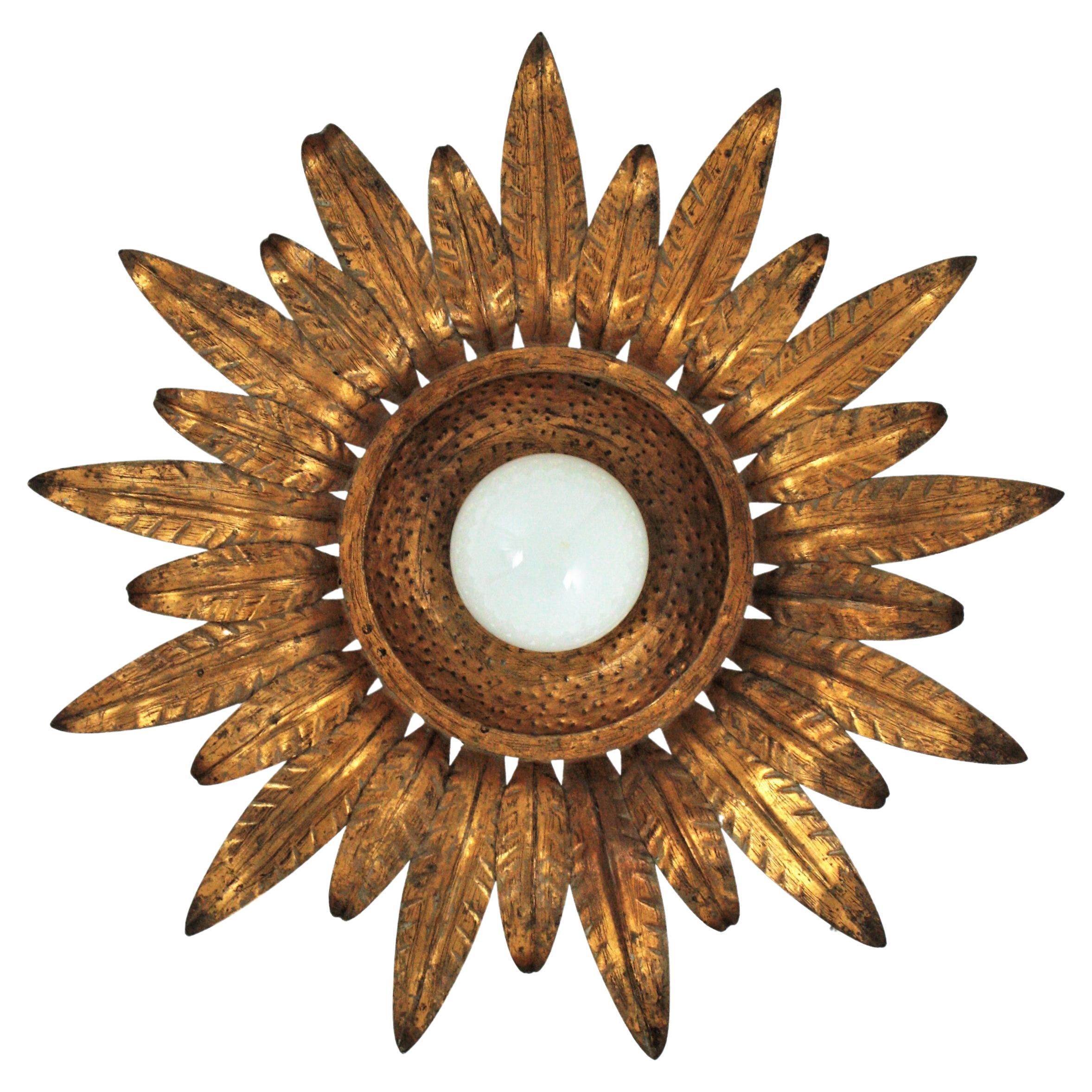 Gilt sunburst leafed light fixture, metal, gold leaf. Spain, 1950s
A hand-hammered gold gilt iron sunburst flower shaped ceiling light fixture with central exposed bulb.
Richly decorated by the hammer marks thorough. It has alternating leaves in