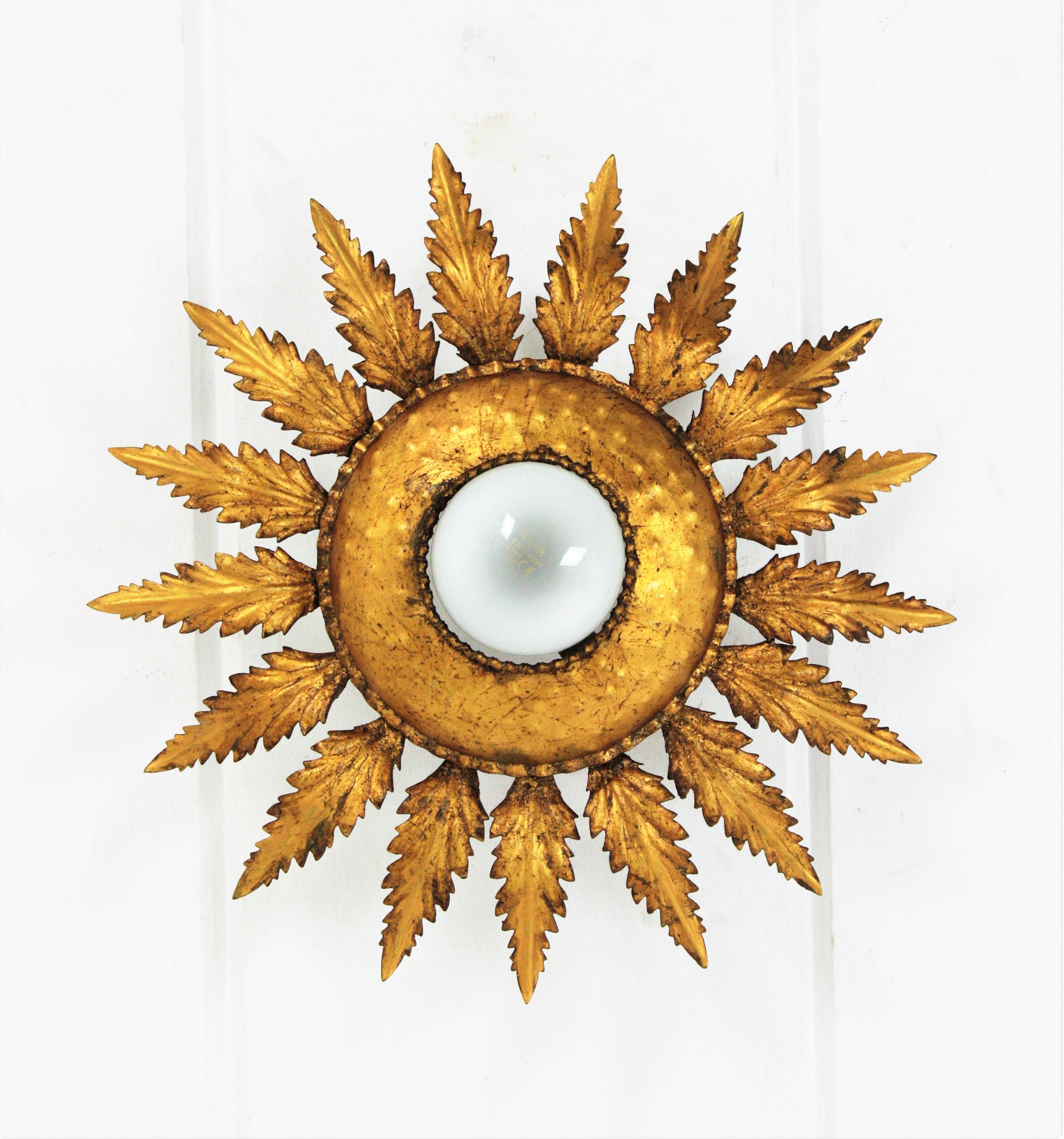 French flower sunburst flush mount, gilt iron, 1950s.
This ceiling light features a frame of leaves surrounding a central exposed bulb. Handcrafted in iron and gilded with gold leag. It has a nice patina.
This sunburst light fixture can be placed