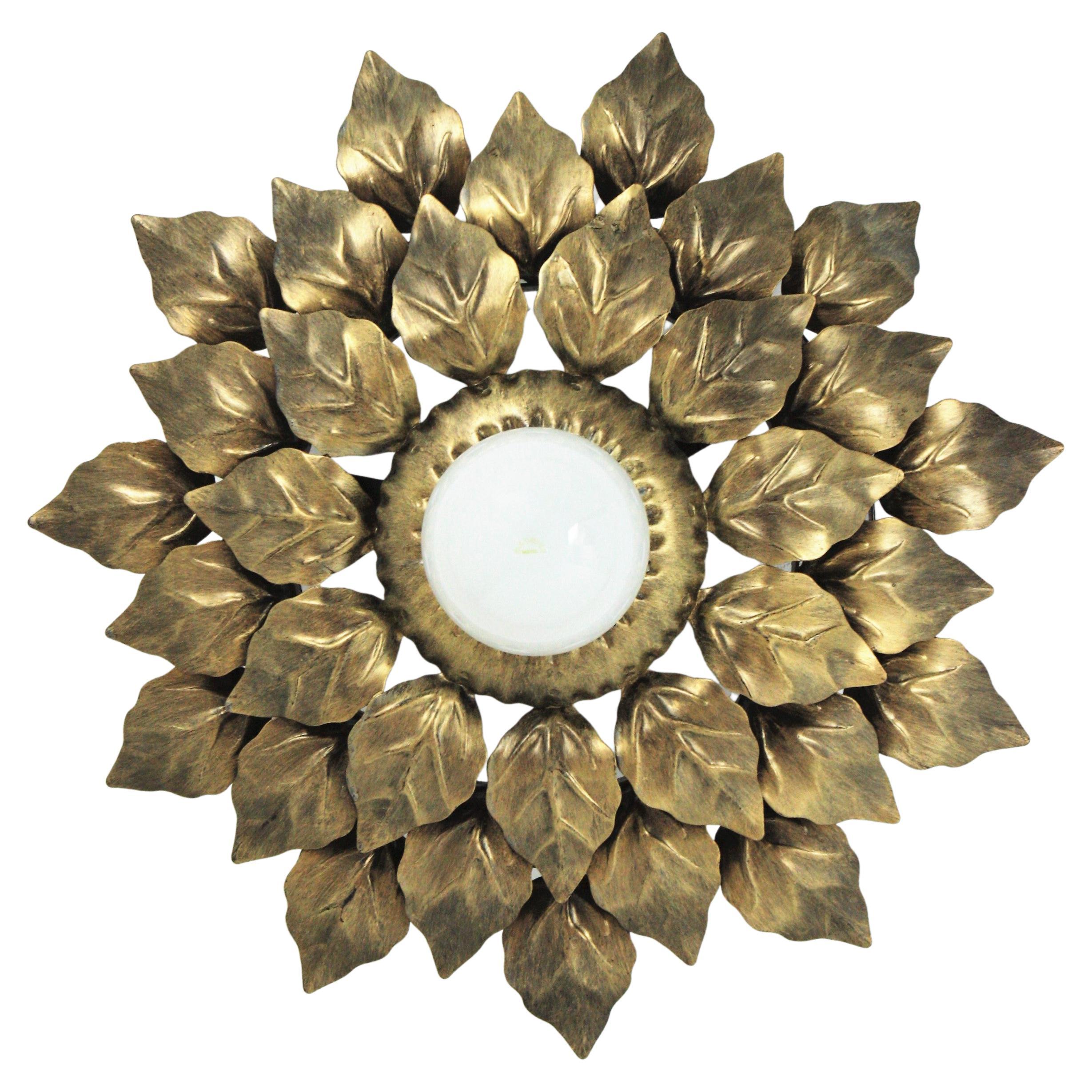 Gilt metal triple layered leafed sunburst ceiling flush mount. Spain, 1960s.
An eye-catching sunburst or flower burst ceiling flush mount with three layers of gilt silvered leaves surrounding a central exposed bulb.
It can be placed flush mounted or
