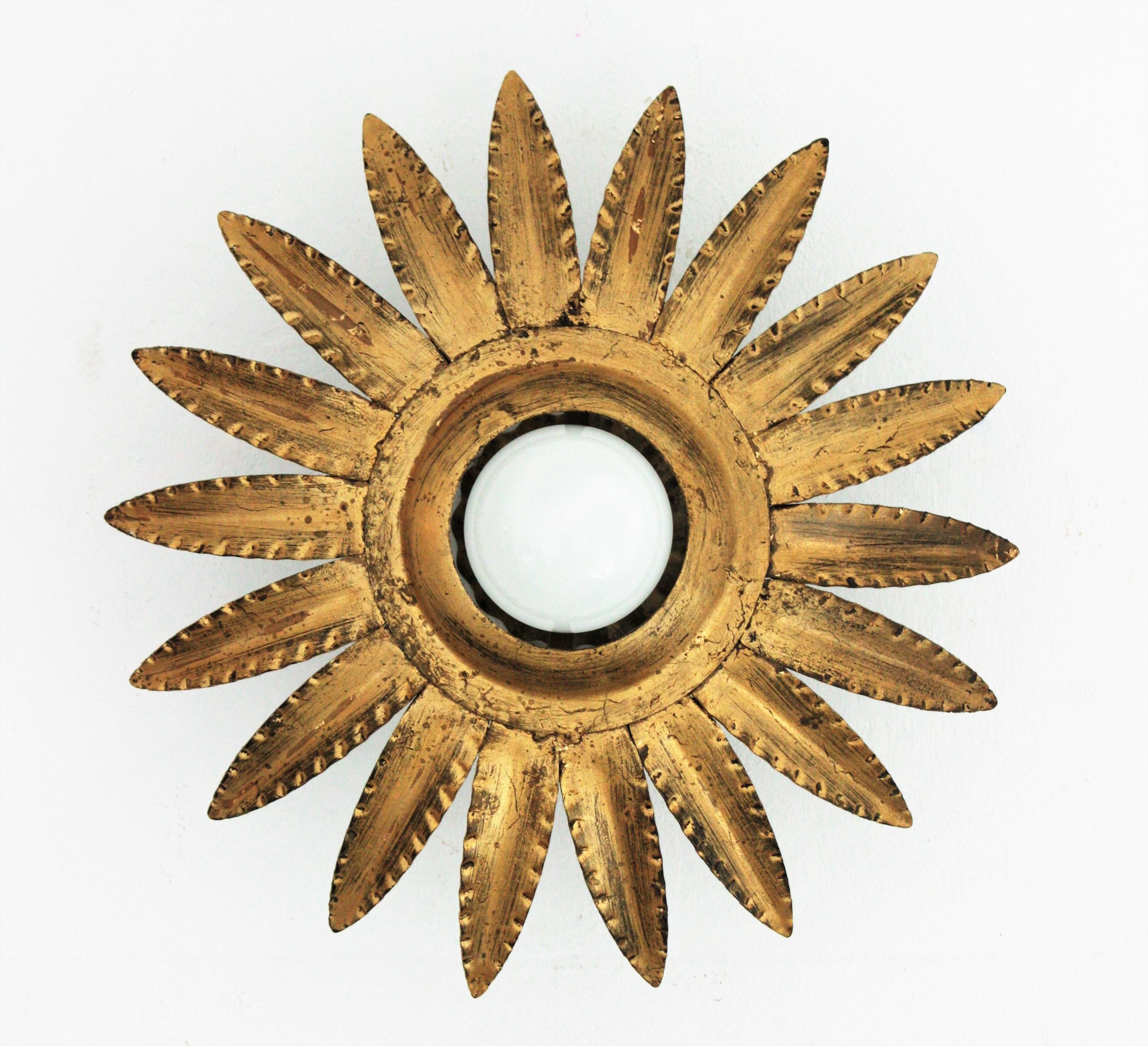 Eye-catching gilt wrought iron sunburst or flower shaped ceiling light fixture, wall sconce or pendant, Spain, 1960s.
A sunburst or flower shaped frame surrounds a central exposed bulb. It has gold leaf gilding and a terrific aged patina.
This