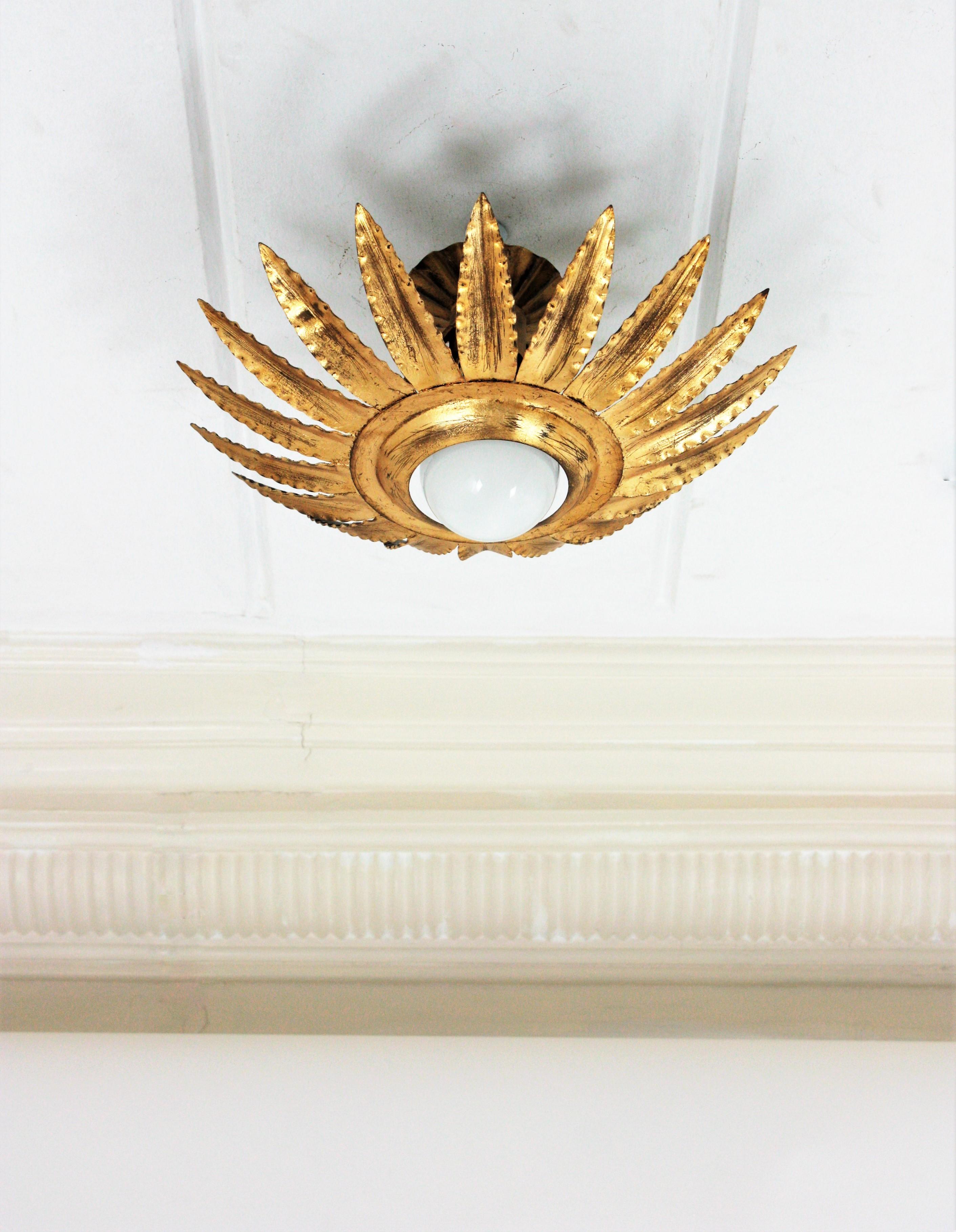 Eye-catching gilt wrought iron sunburst or flower shaped ceiling light fixture, wall sconce or pendant, Spain, 1960s.
A sunburst or flower shaped frame surrounds a central exposed bulb. It has gold leaf gilding and a terrific aged patina.
This