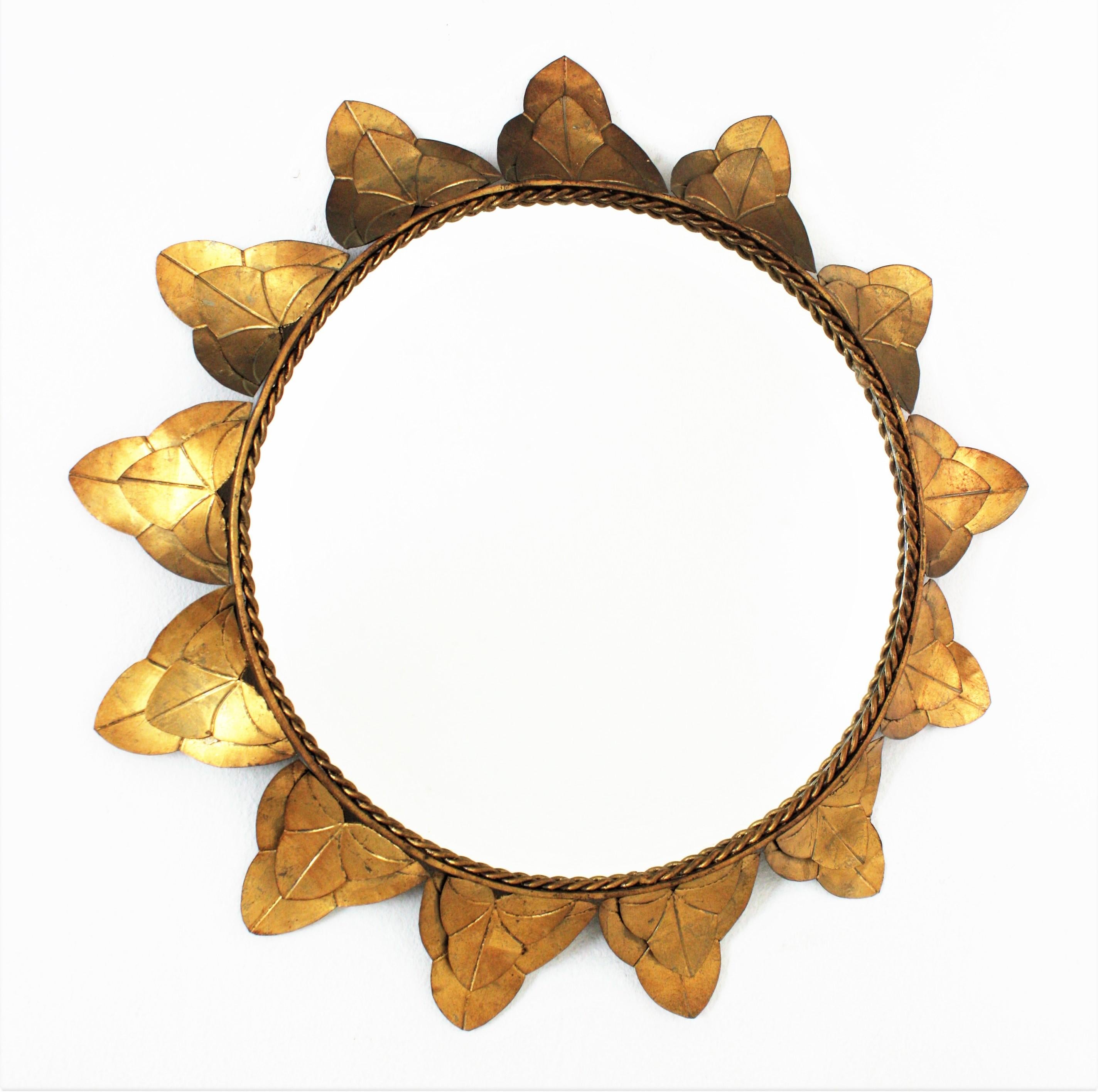 Handcrafted gilt metal sunburst mirror, Spain, 1950s.
This beautiful sunburst mirror has a frame with a double layer of iron leaves surrounding a central mirror glass. Each leaf is adorned by engraved decorative details. It has a nice patina with