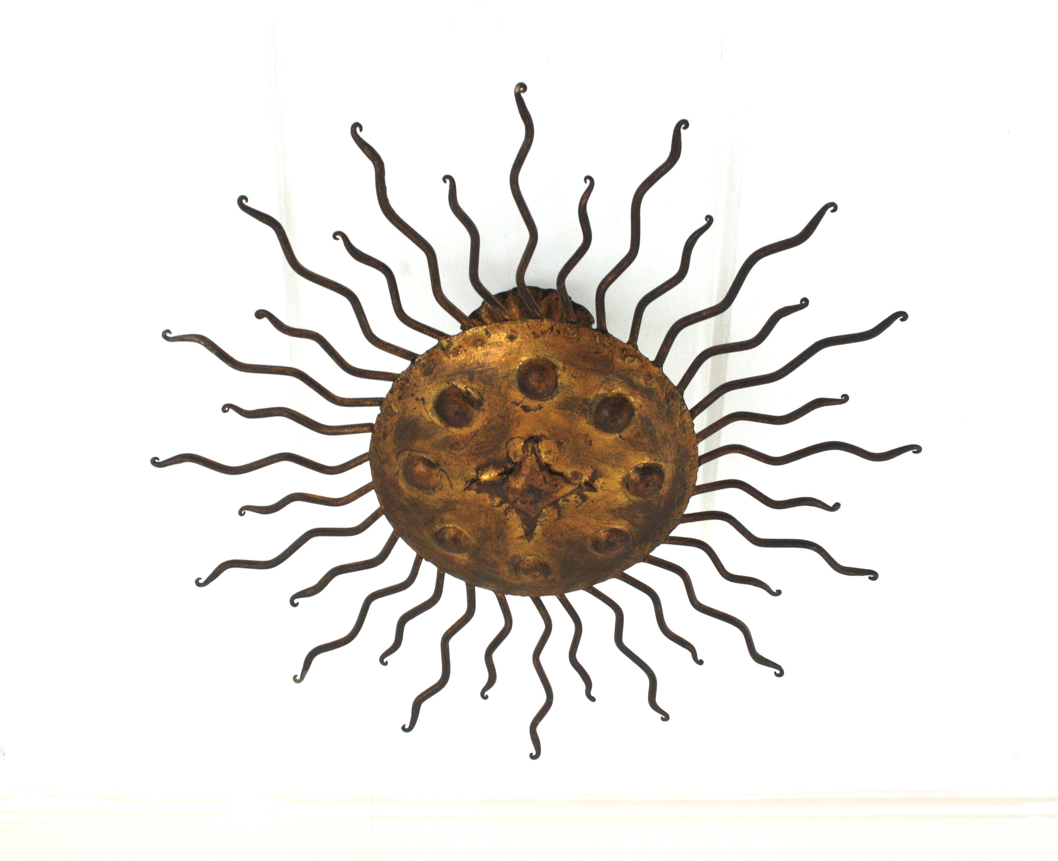 Eye-catching gilt wrought iron sunburst ceiling flush mount in the style of Brutalism. Manufactured by Ferro Art, Spain, 1940s-1950s.
Nicely adorned by hammered bubbles at the central sphere and curly rays surrounding it. It has a terrific aged