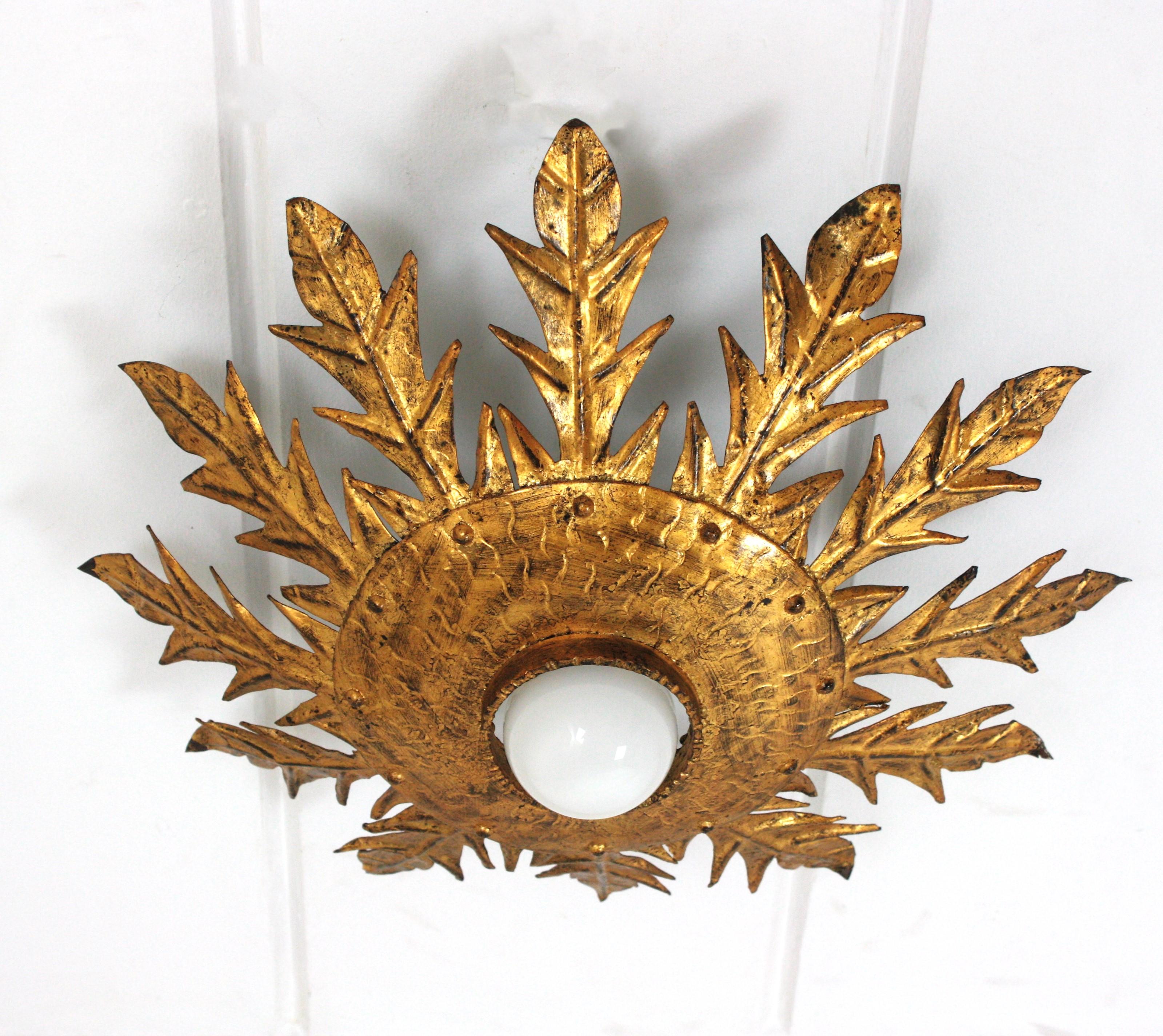 Eye-catching french sunburst foliage flush mount in gilt iron, 1950s.
This leafed sunburst ceiling light fixture has a beautiful construction with twelve large leaves surrounding a central hand-hammered ring with nail accents.
It has a central