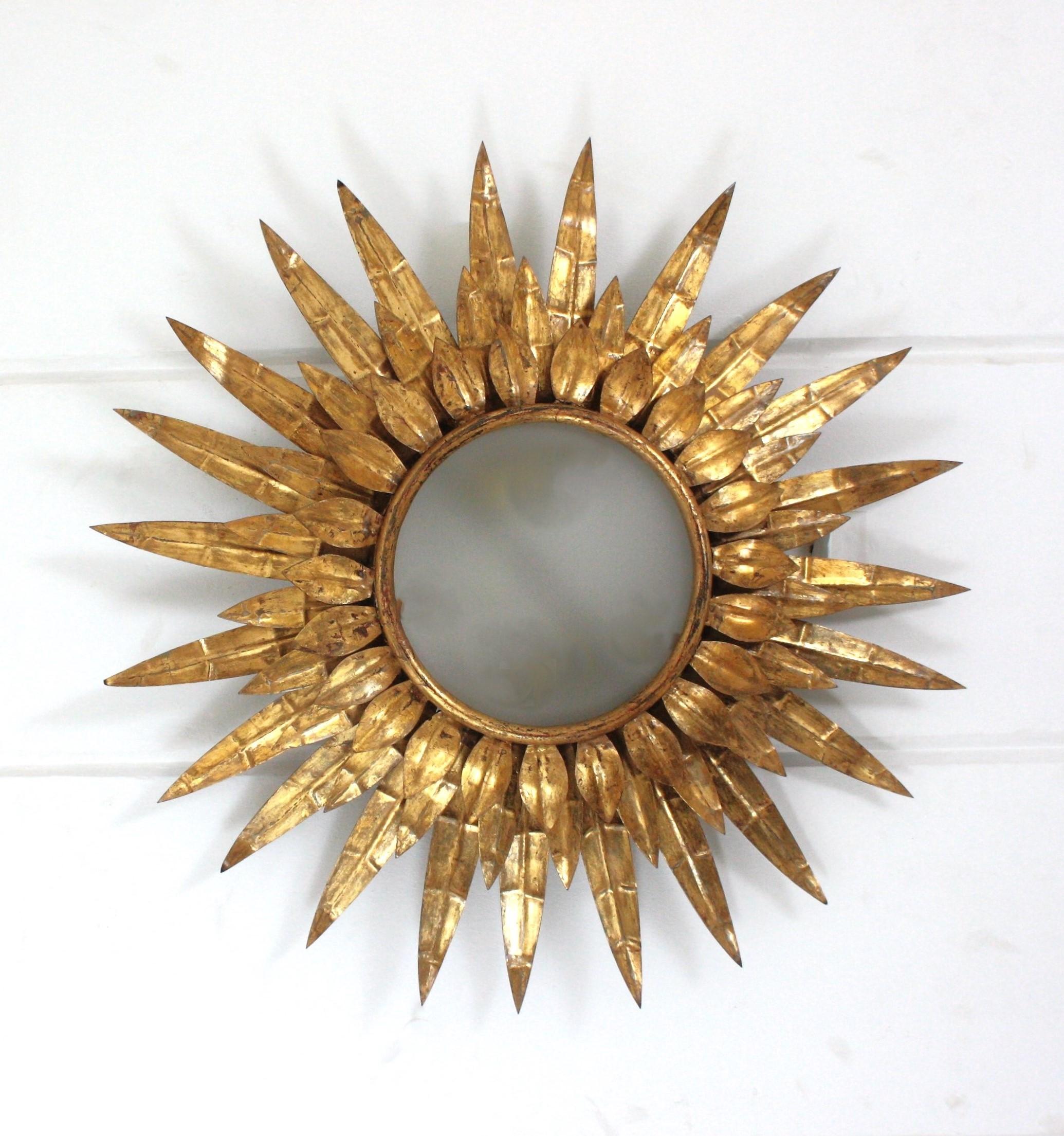 Lámpara de techo empotrable de hierro dorado y cristal con marco de hojas. Francia, años 50.
Esta luminaria con forma de rayo de sol presenta una triple capa de hojas / rayos que rodean un panel central de cristal esmerilado. Cada capa tiene rayos