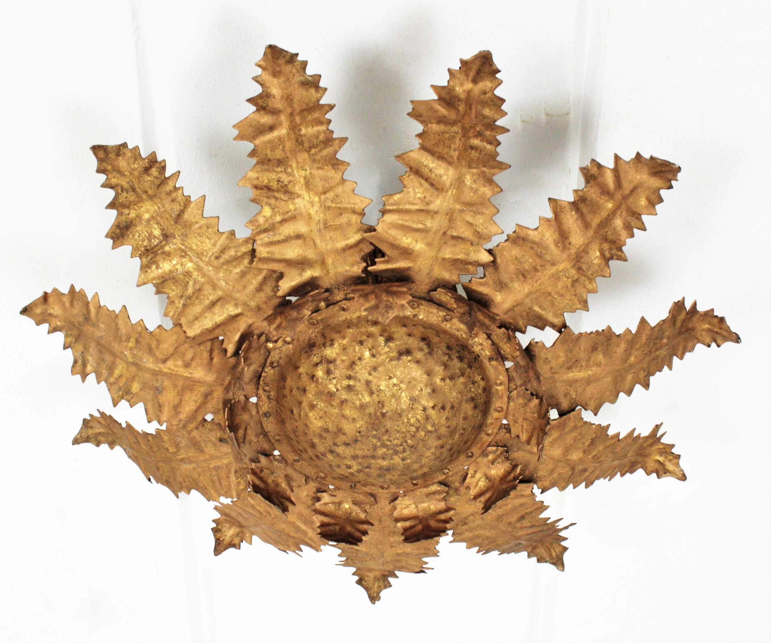 Terrific handcrafted gold gilt wrought iron sunburst leafed flush mount ceiling light. France, 1950s.
This ceiling light fixure has a foliate sunburst or flower burst design with a richly hammered work thorough. 
It shows an exquisite