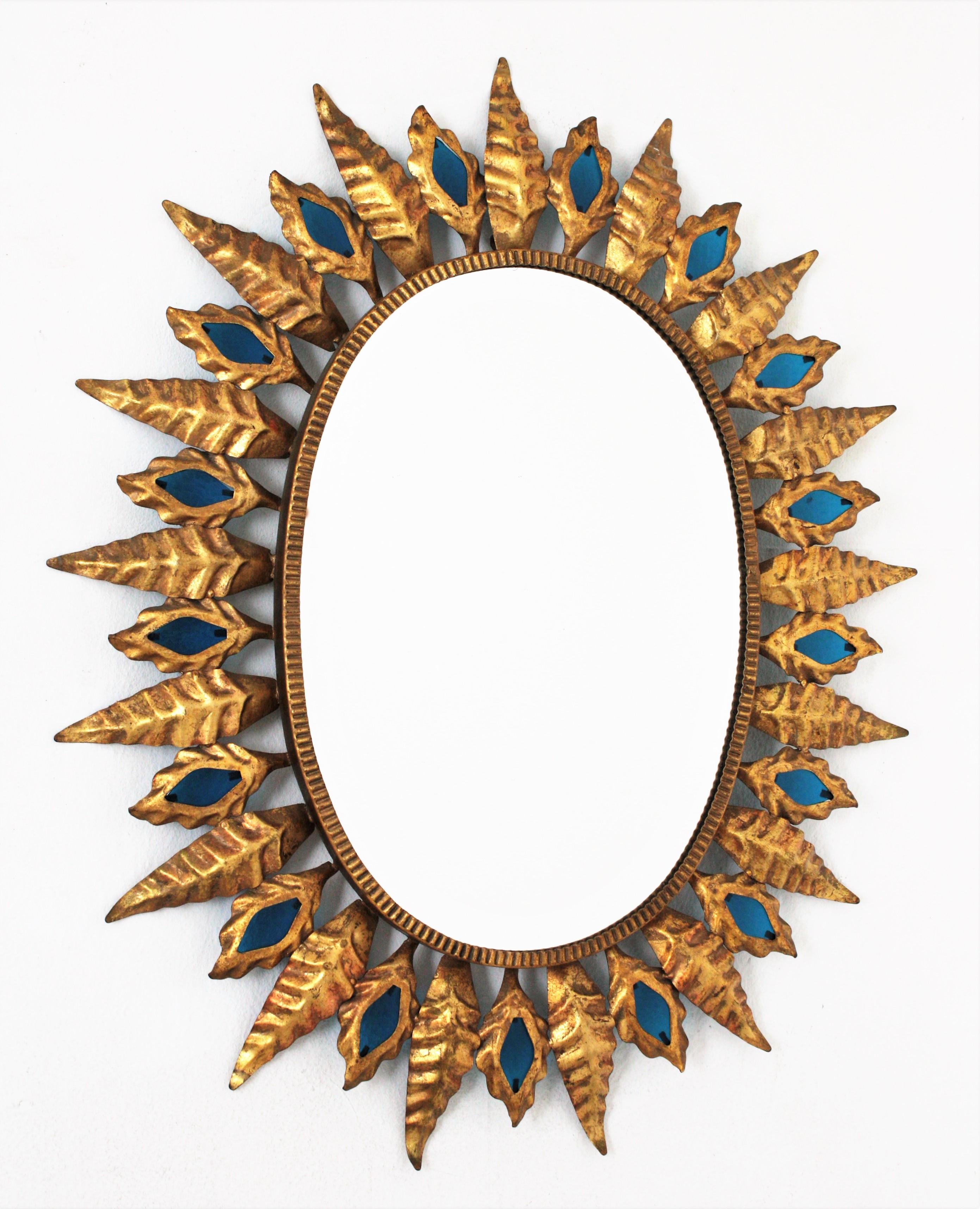 Blue glass and gilt metal oval sunburst mirror in the Hollywood Regency style, Spain, 1960s.
This oval sunburst mirror features a leafed frame with alternating large and small leaves accented by Classic blue glasses.
Blue is the color of the year