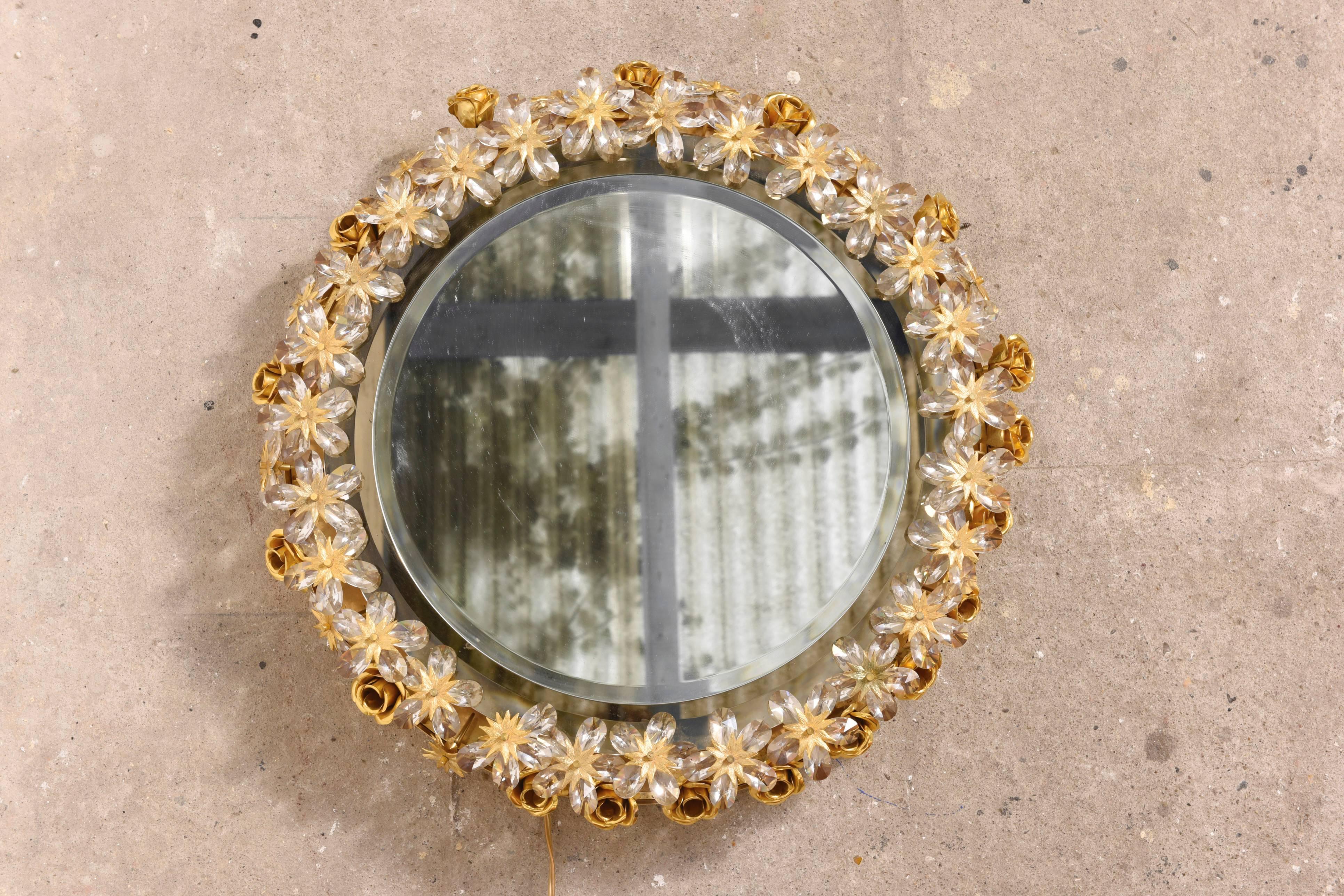 Beautiful brass illuminated mirror Made by Palwa, Germany with original label. The large individual flower has jewel-like faceted crystals set in a brass circle enclosing the mirror with one row of gilded roses. The lighting through the crystals