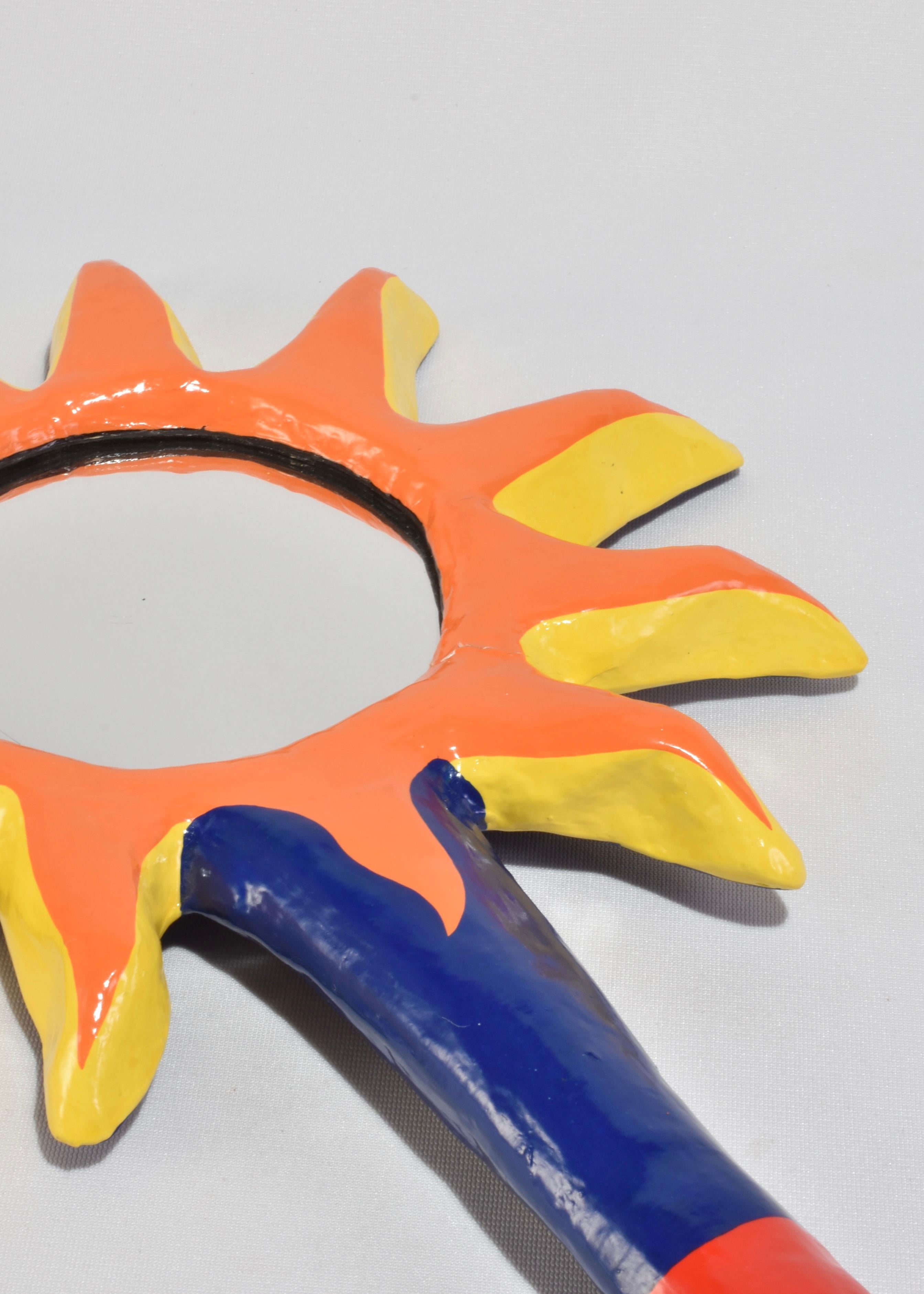 Handgefertigter Spiegel mit einer kühnen Sonnenschliff-Silhouette in lebhaften Orange-, Gelb-, Rot- und Kobalttönen. Geformt aus leichtem Pappmaché mit glänzender Oberfläche. Die Rückseite ist mit einem wirbelnden Spiralmotiv in tiefem Marineblau