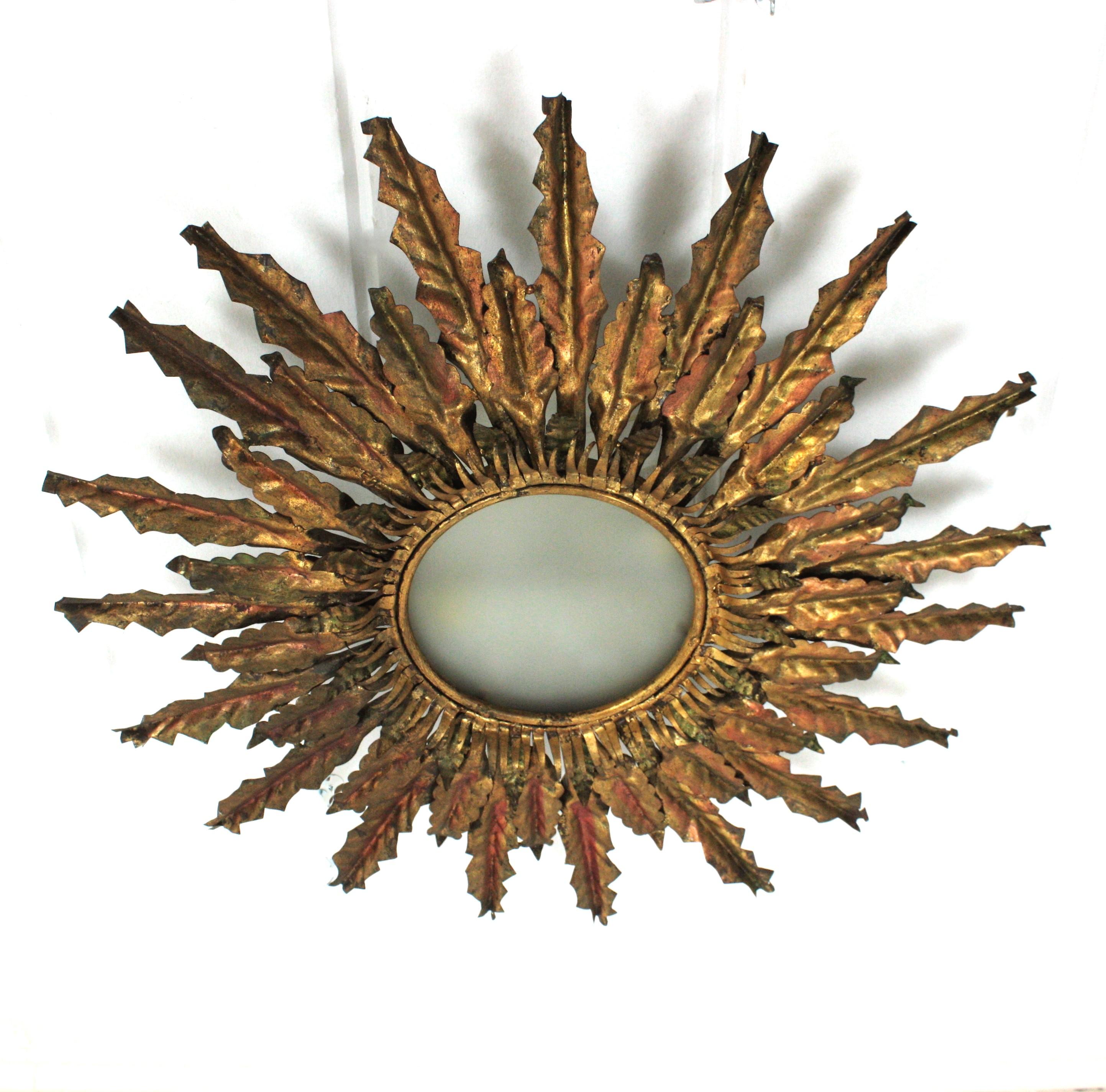 Monumental richly decorated extra large (35 in) hand hammered gold gilt iron sunburst light fixture. Spain, 1940s. 
It has double set of leaves in two sizes around a corolla with small leaves surrounding a central frosted glass light diffuser. 
The
