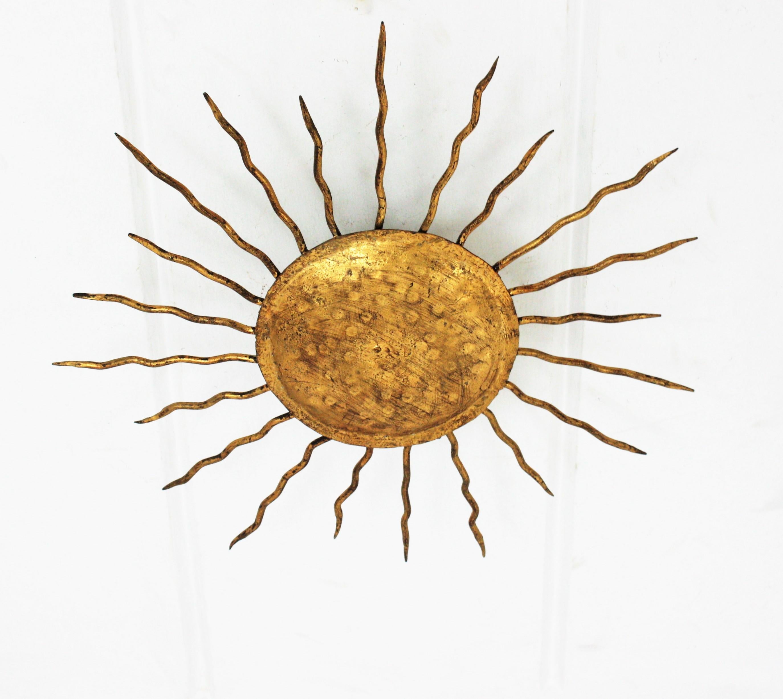 Spanische mittelgroße Leuchte aus handgehämmertem, vergoldetem Eisen mit Sonnenschliff aus der Zeit des Brutalismus. Spanien, 1960er Jahre.
Es hat gelockte Eisenstrahlen in zwei Größen, die die zentrale Kugel umgeben. Schön als Deckenleuchte und