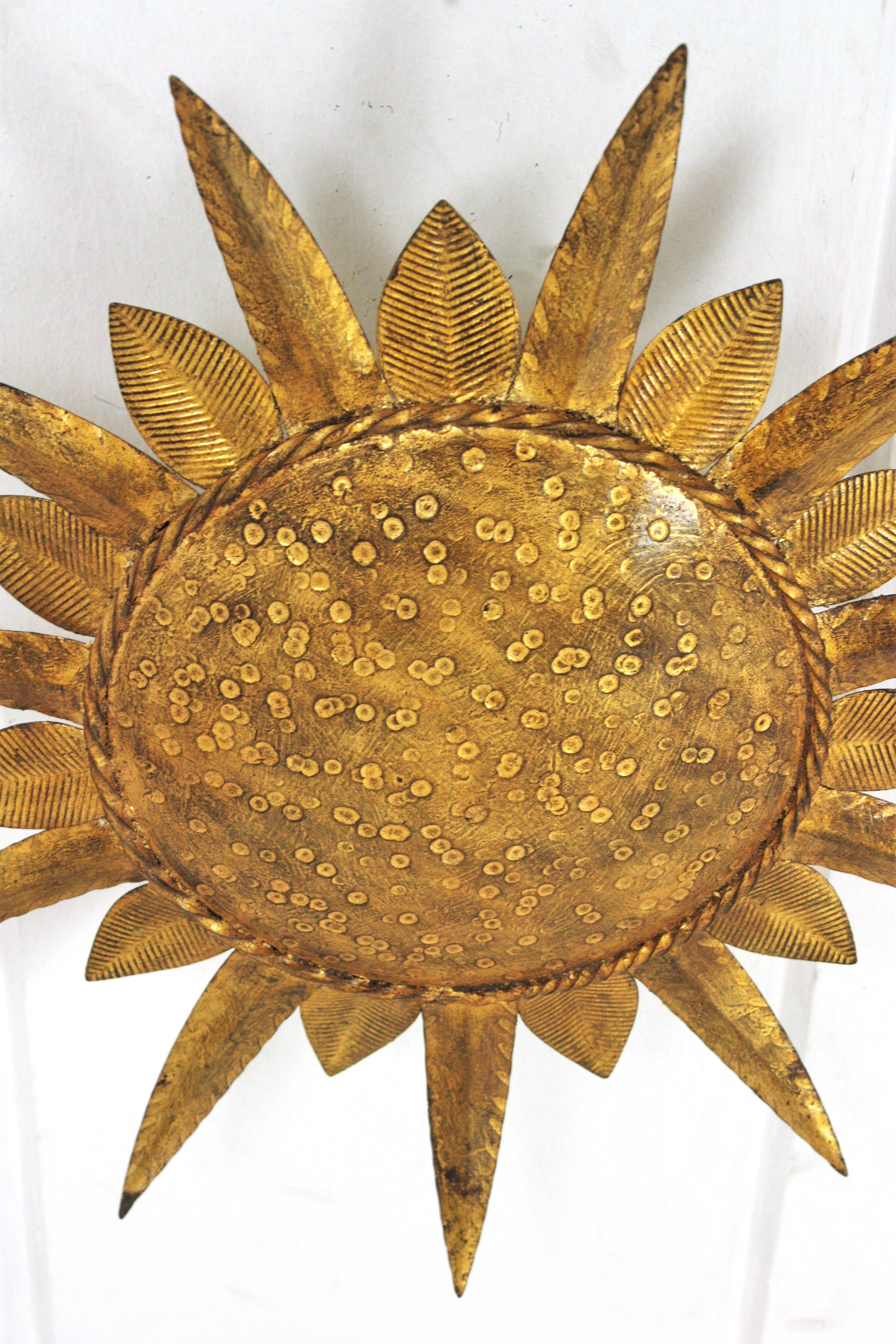 Eye-catching gold leaf gilt iron leafed sunburst flush mount. Manufactured by Ferro-Art. Spain, 1950s-1960s.
This ceiling flushmount features an iron structure with a central round panel framed by alternating short and long leaves
The central part