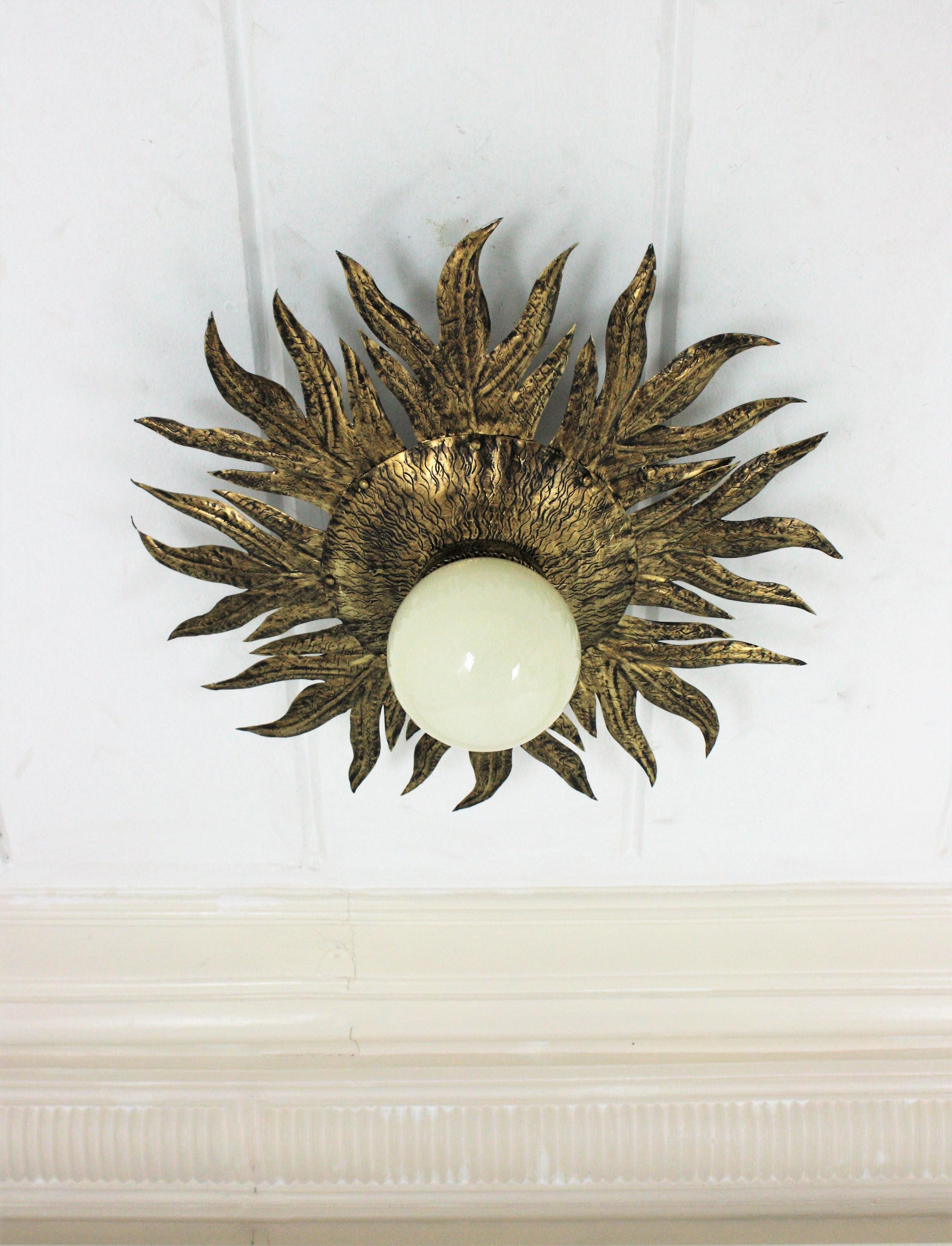 Brutalist gilt metal sunburst ceiling flush mount with milk glass globe shade. Spain, 1960s.
This gilt iron sunburst light fixture with opaline globe shade was manufactured in Spain at the Mid-Century Modern period in the style of Brutalism.
It