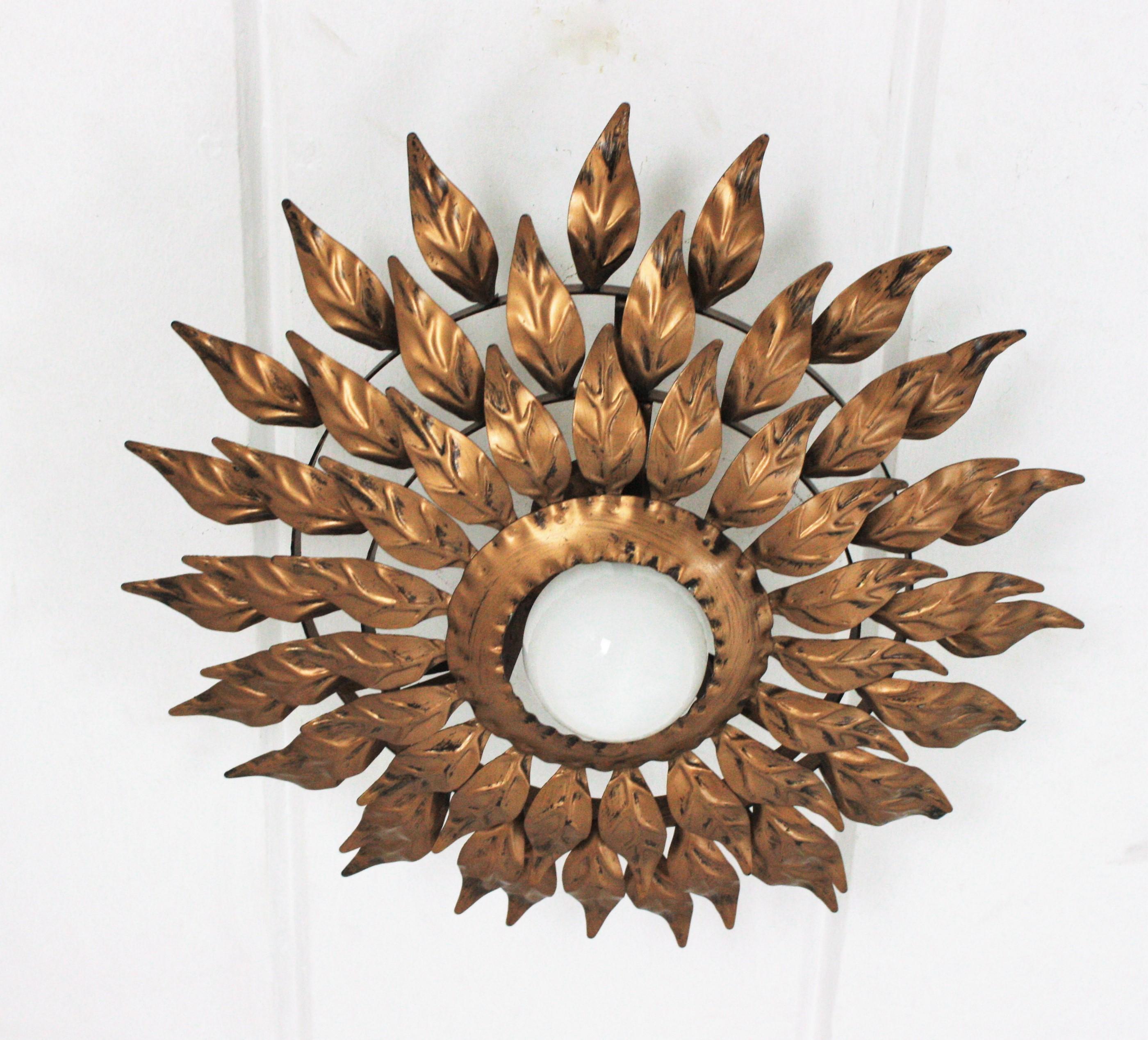 Gilt metal triple layered leafed sunburst ceiling flush mount. Spain, 1960s.
Three layers of leaves
An eye-catching sunburst or flower burst ceiling lamp with three layers of small gilt iron leaves surrounding a central exposed bulb.
It can be