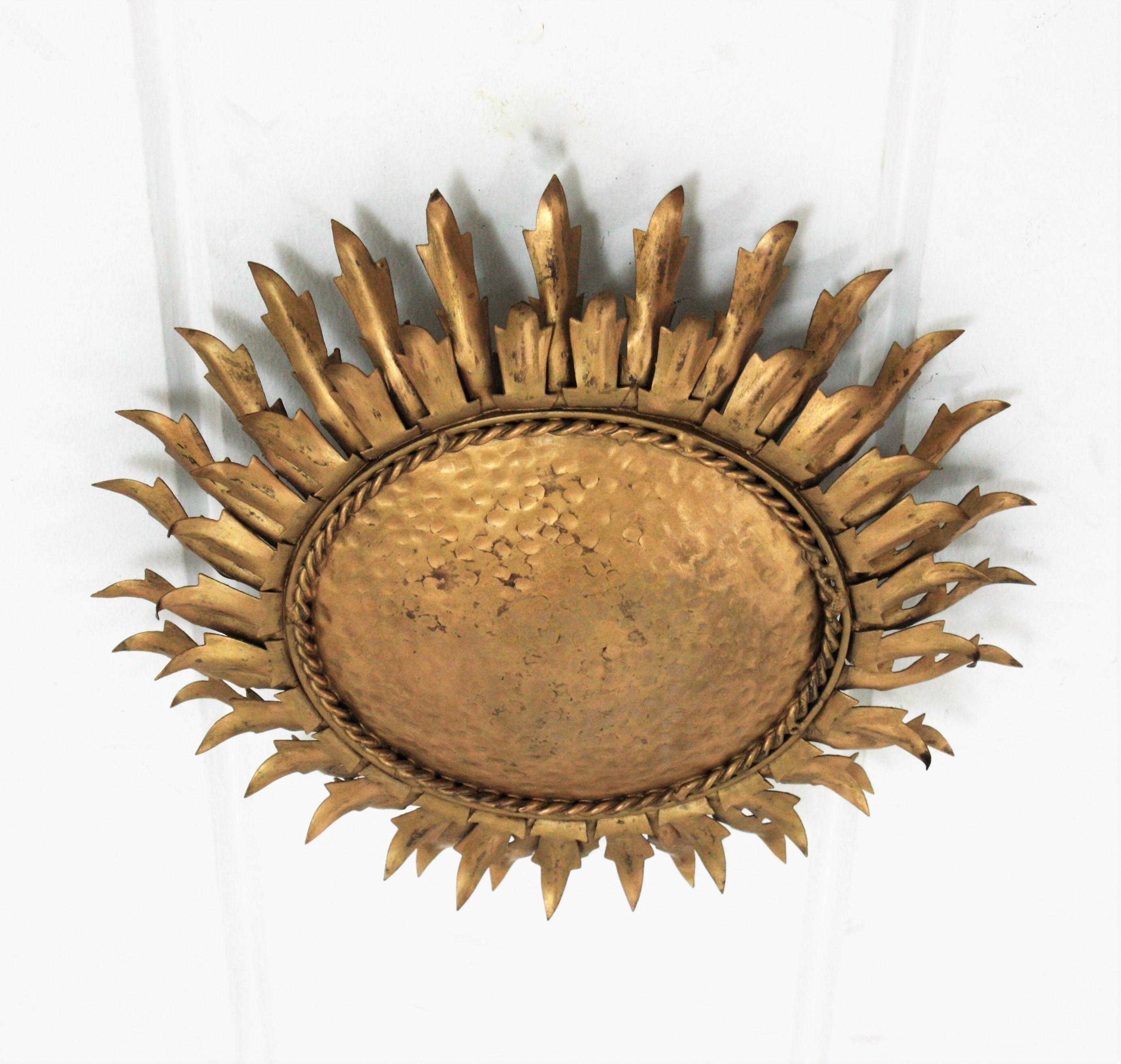 Eye-catching gilt iron leafed sunburst flush mount. Spain, 1950s-1960s.
This ceiling light fixture features an iron structure with a central round panel framed by two layers of iron leaves.
The central part is heavily adorned by the hammer marks