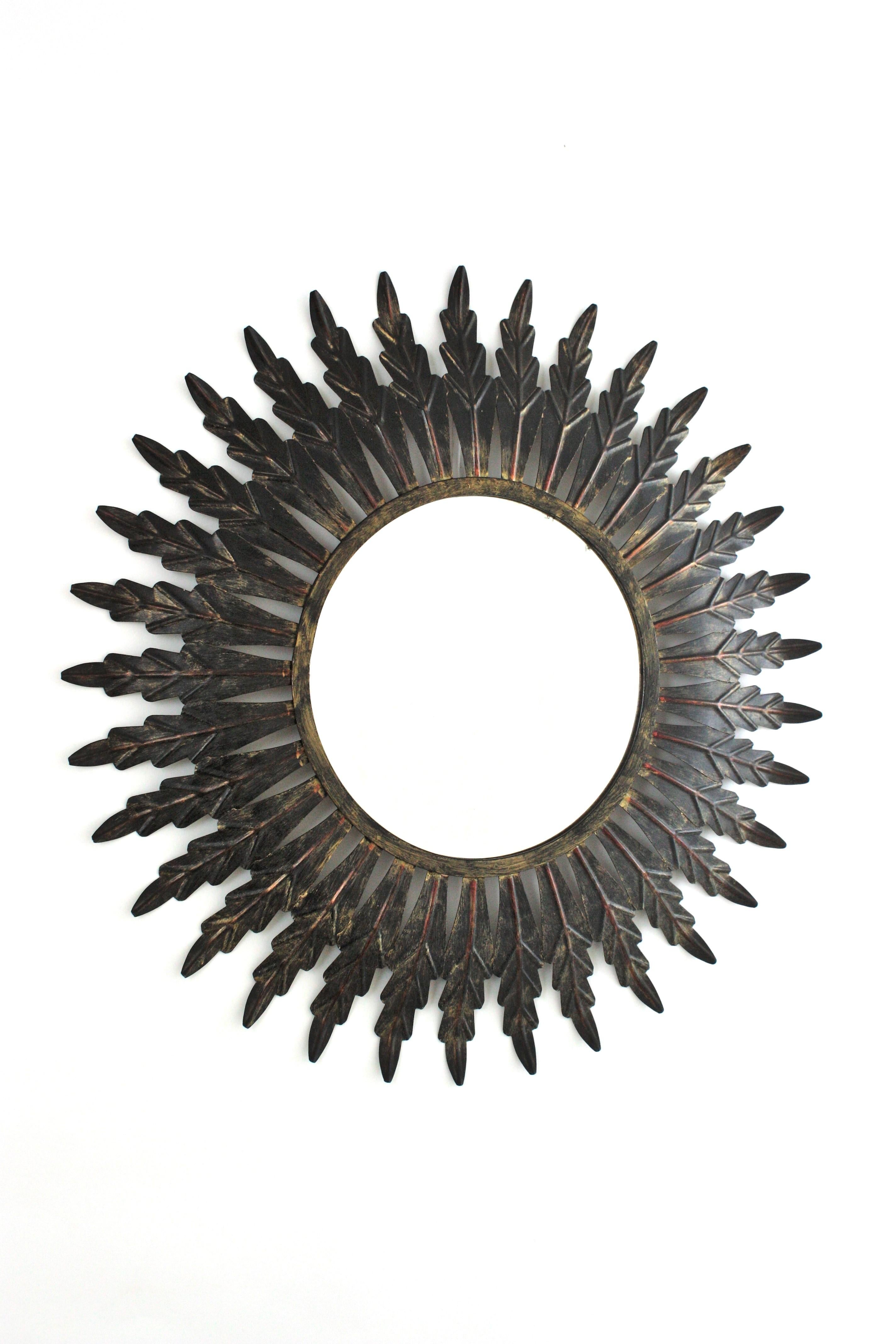 Sunburst mirror handcrafted in iron with black patinated finish, Spain, 1960s.
The frame of this wall mirror features a layer leaves surrounding a central round glass.
This iron sunburst mirror has been finished in a black patina to add a modern