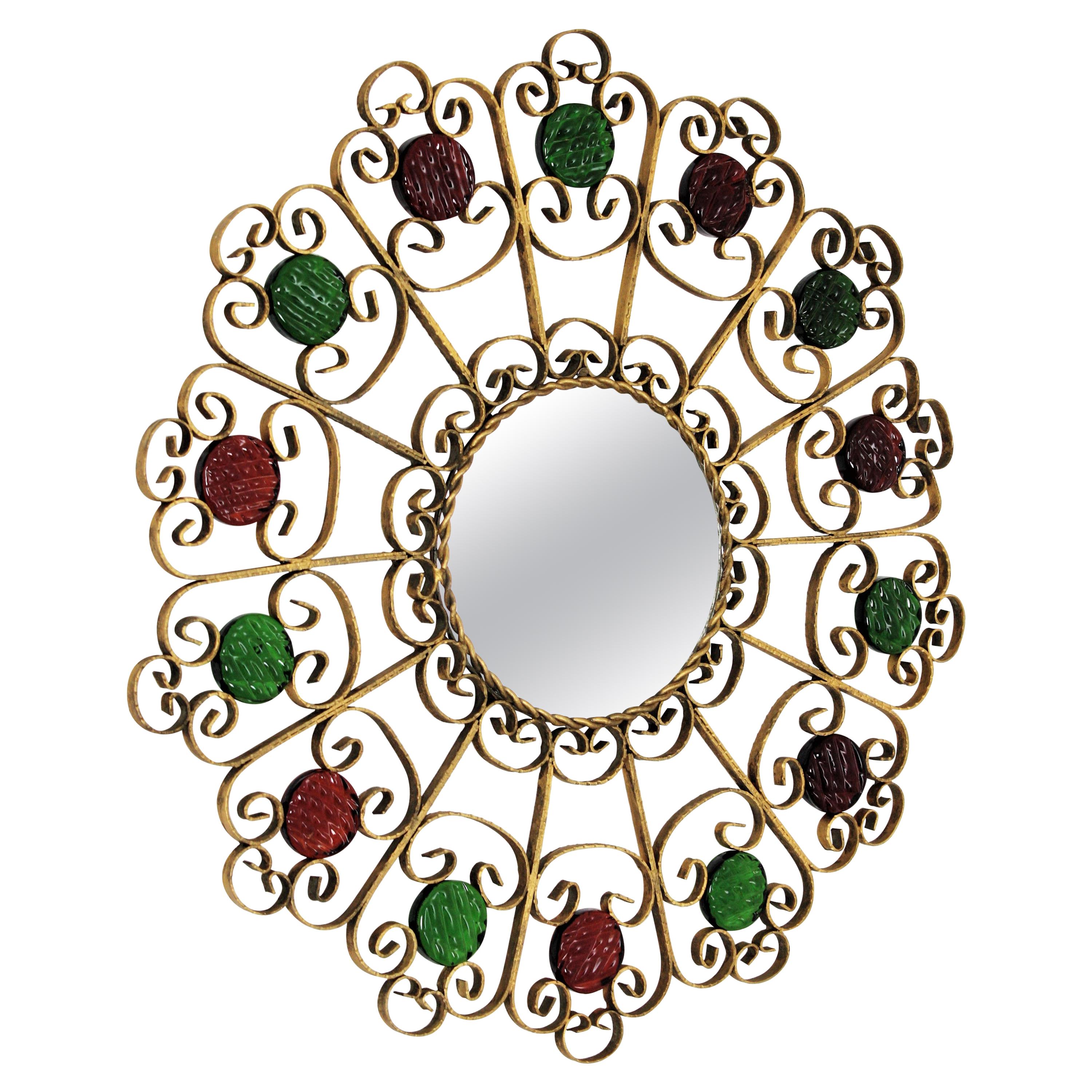 Spanish wrought iron scrollwork mirrorr accented by red and green glasses

Beautiful wrought gilt iron scroll motif mirror framed with garnet and green glasses, Spain, 1950s.
The frame shows the Spanish traditional wrought iron work: it is richly