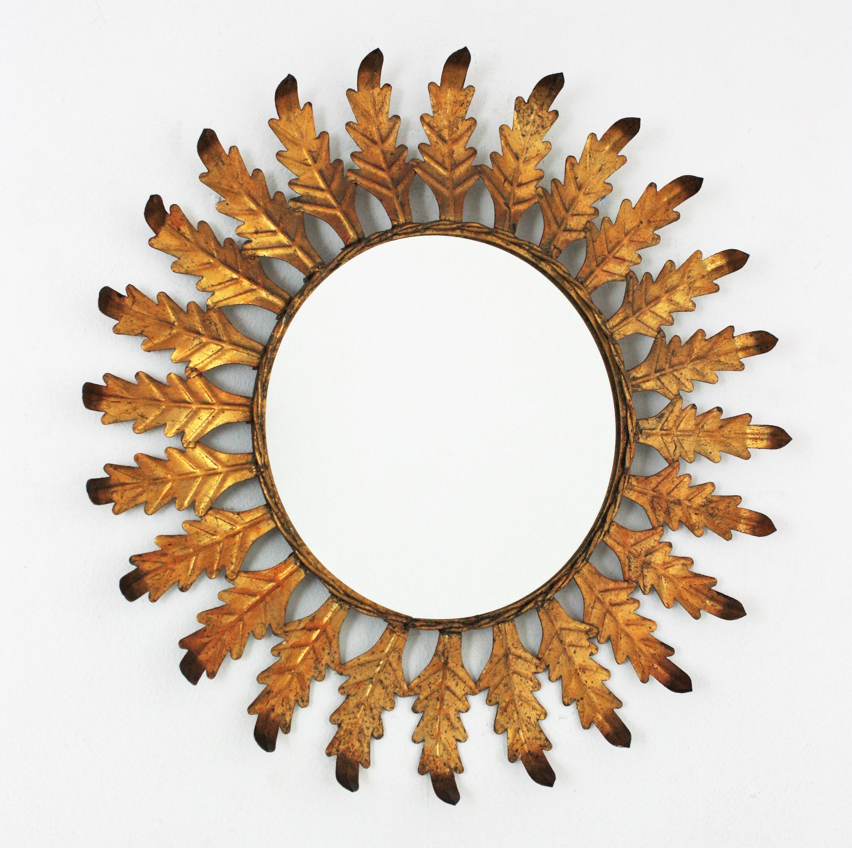Sunburst Mirror with leaves frame, gilt iron, Spain, 1960s.
This eye-catching wall mirror has a leafed sunburst frame finished with gold leaf gilding and darker accents on the leaf endings. 
Nice aged patina and original gilding. 
Overall