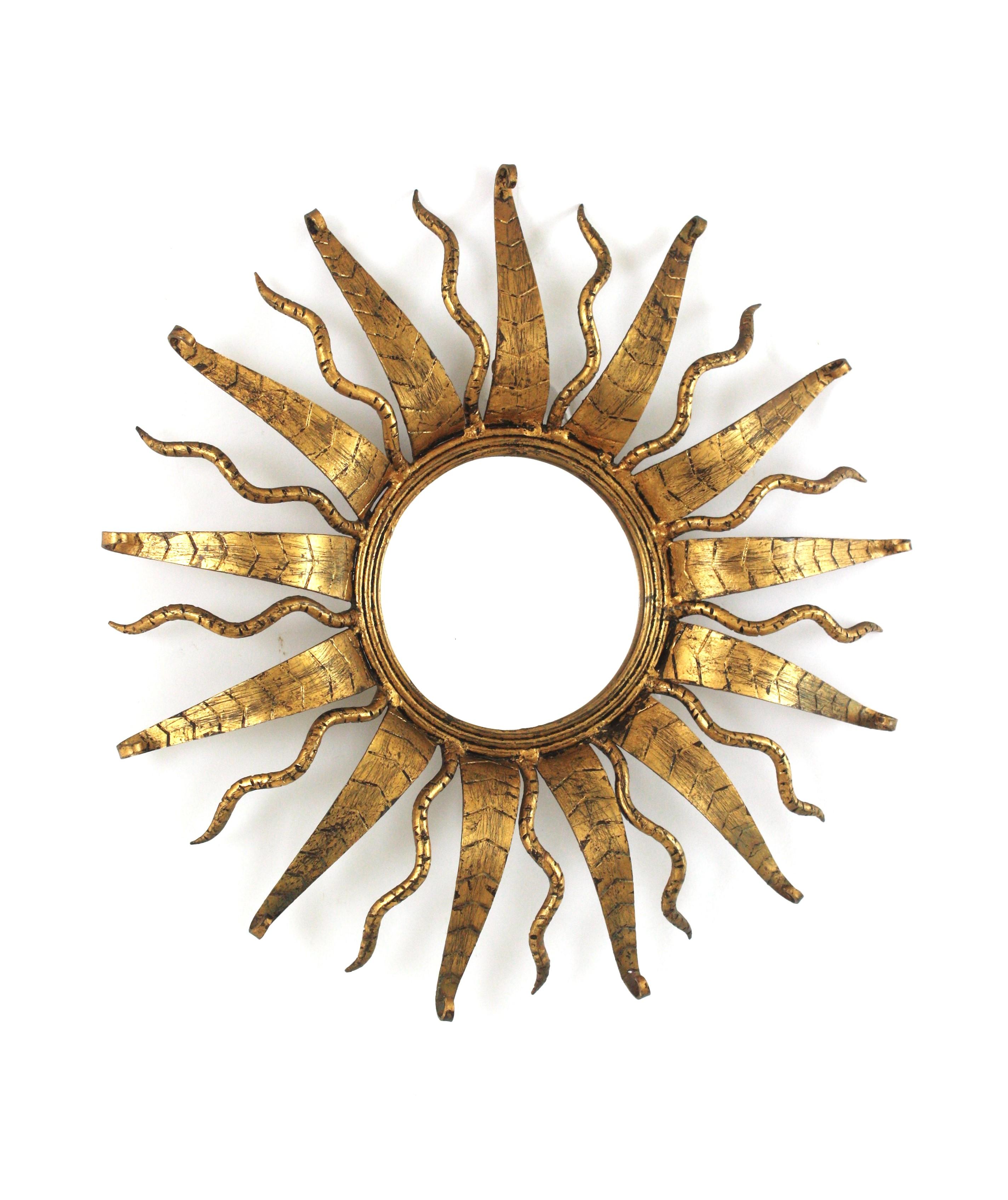 Espejo Español Sunburst de Hierro Forjado Dorado en Pan de Oro
Espejo de pared redondo de hierro forjado dorado de la modernidad de mediados de siglo, España, años 50.
Este espejo sunburst presenta un anillo que enmarca el cristal redondo central y