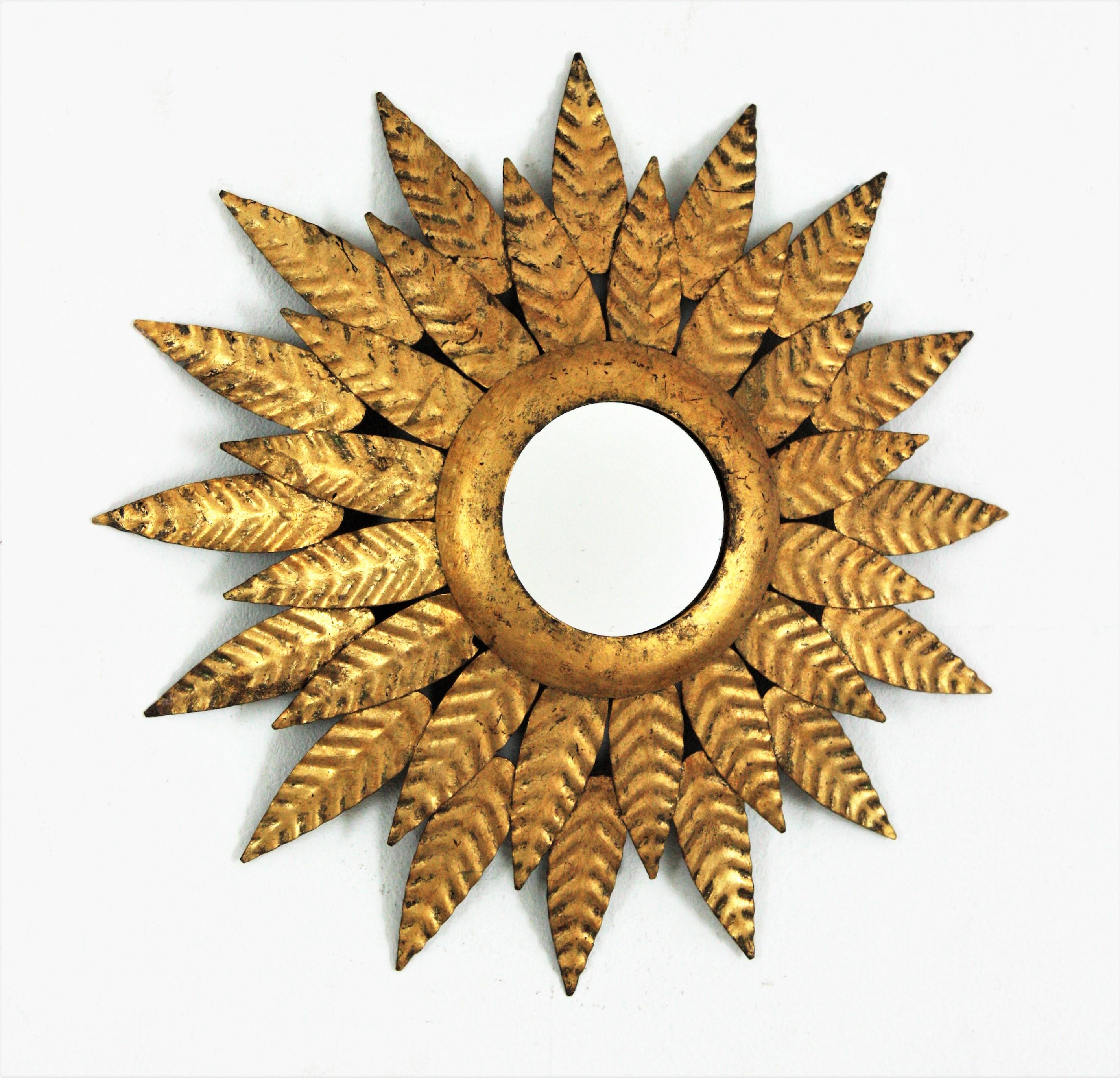Mid-Century Modern double layered sunburst round wall mirror with gold leaf finish. Spain, 1950s.
Double layer of hand hammered leaves surrounding the central glass. Each leave is nicely adorned by the hammer work.
This highly decorative leafed
