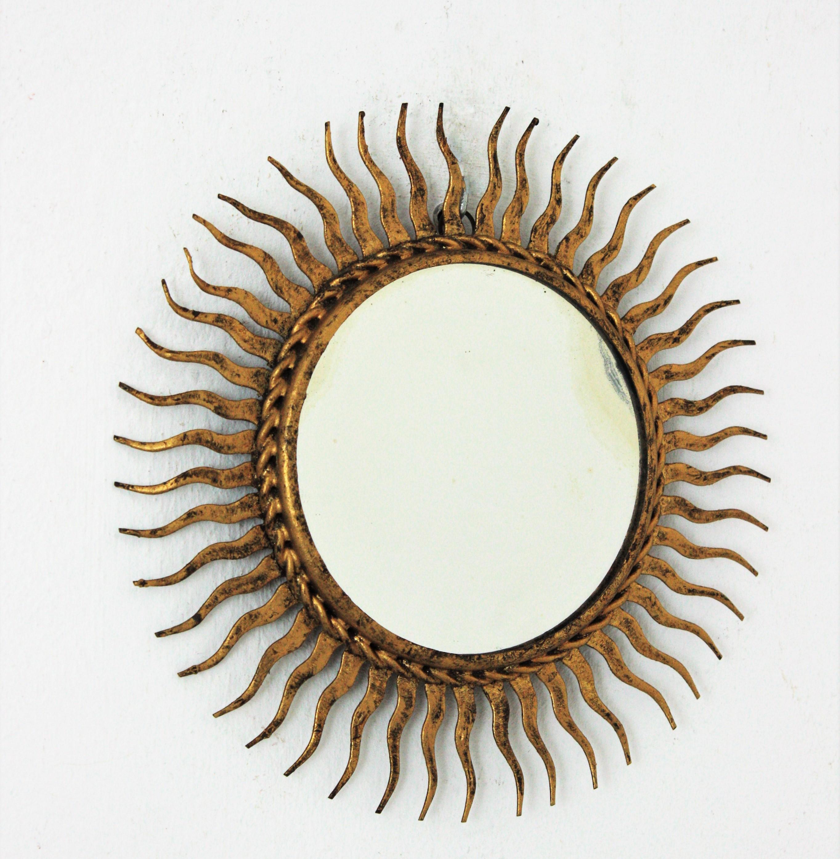 Mid-Century Modern mini sized wrought gilt iron sunburst mirror. Spain, 1960s.
Hand forged iron finished with gold leaf gilding.
This lovely mirror has a beautiful aged patina according to its age.
Interesting as a part of a sunburst wall