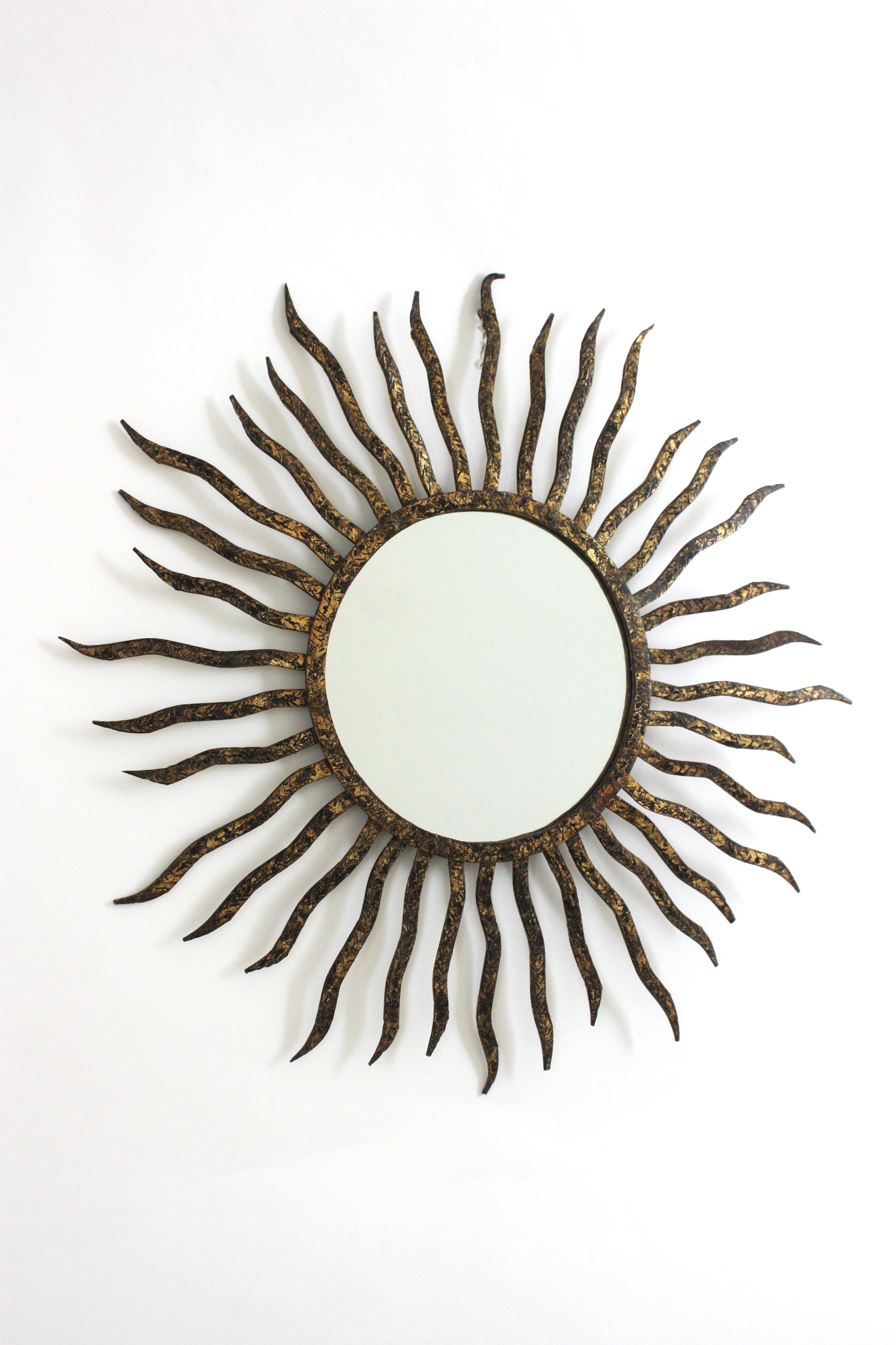 Spiegel mit Sonnenschliff nach Gilbert Poillerat, Paketvergoldetes Schmiedeeisen, Blattgold, Frankreich 1940er Jahre.
Dieser Sunburst-Wandspiegel hat ein auffälliges Sunburst-Design mit Eisenstrahlen in verschiedenen Größen, die ein zentrales Glas
