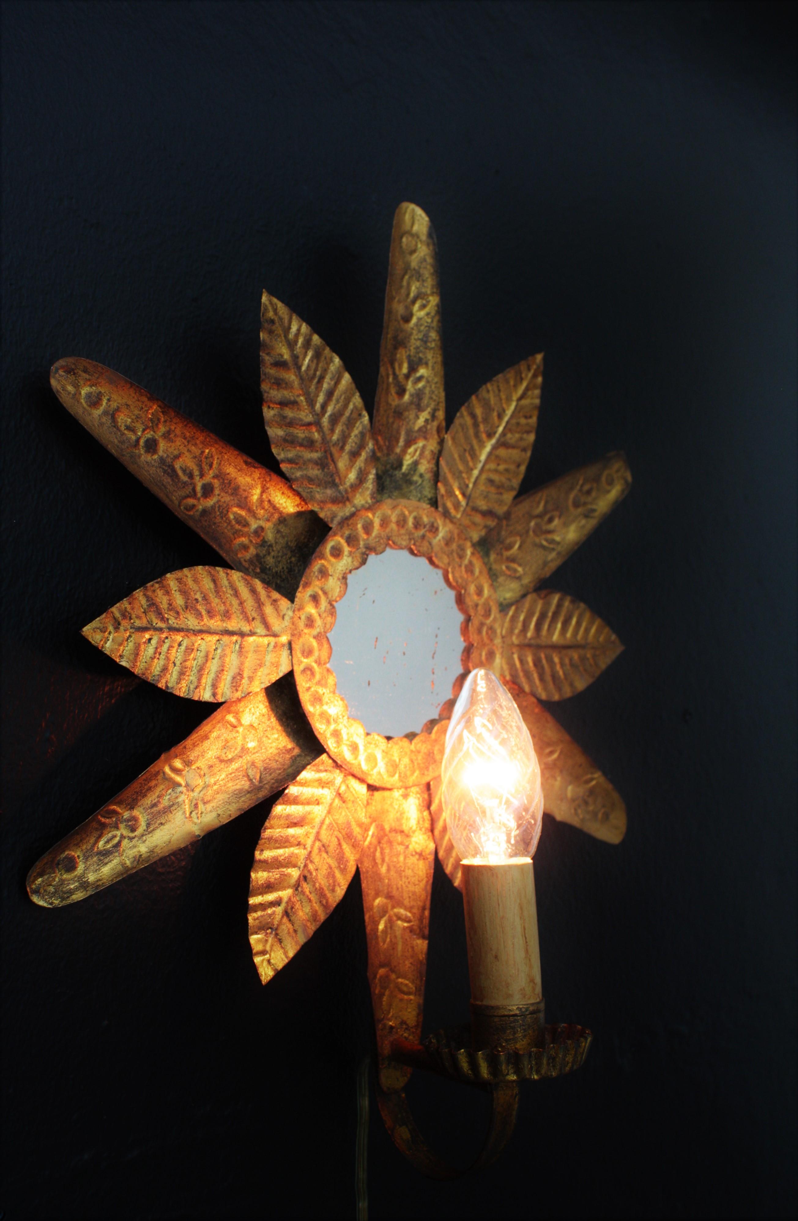 A Hollywood Regency gilt iron sunburst wall sconce. France, 1940s.
Small gilt iron wall sconce sunburst mirror with single light and gold leaf finishing.
This lovely handcrafted metal sunburst mirror has alternating leafs with different hammered