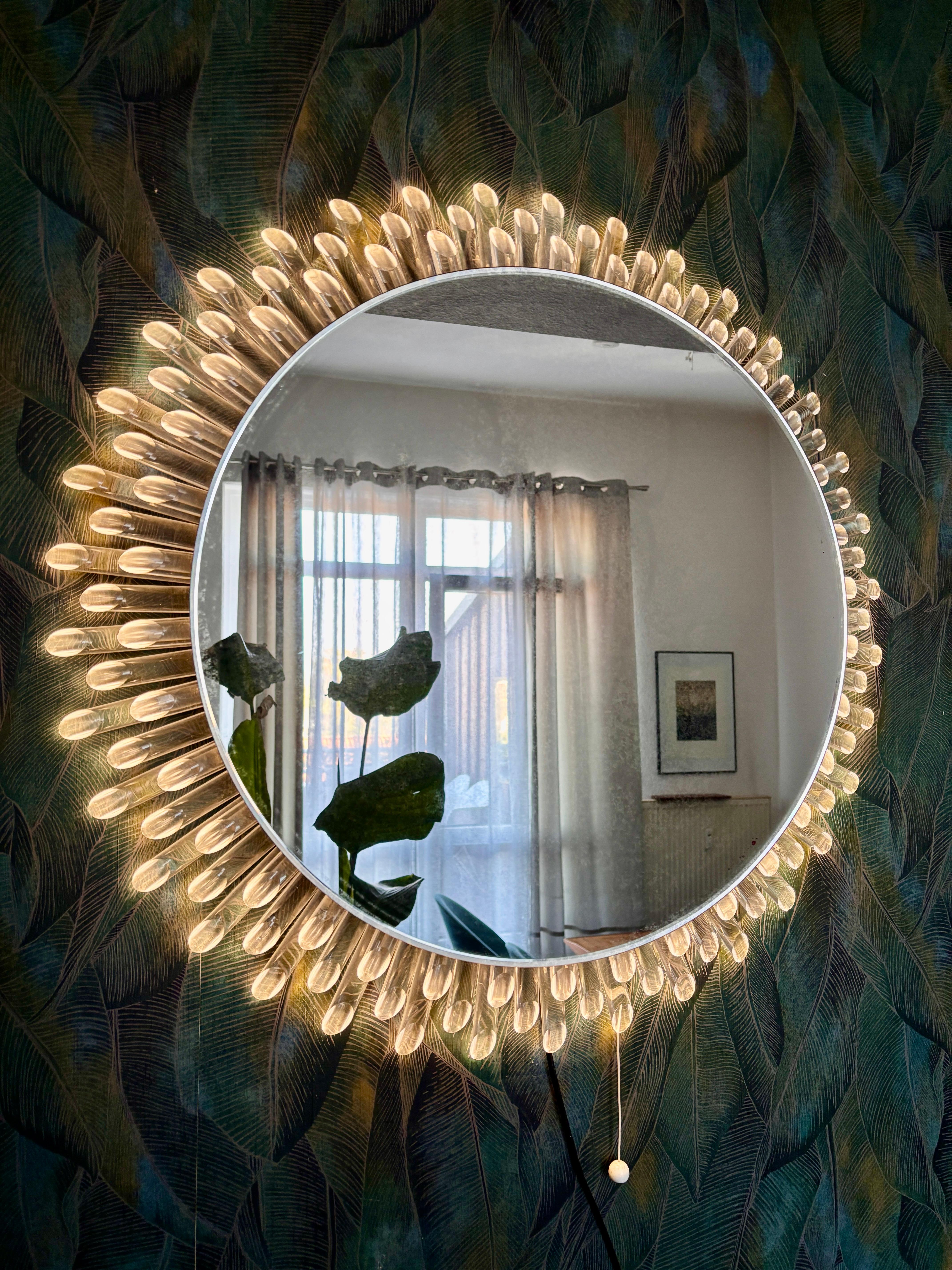 An absolute rarity!
A round sunburst wall mirror with indirect lighting was made in Germany in the 1970s. The round mirror is held by a round aluminum wall bracket and surrounded by three layers of Lucite rods. All rods are intact. The mirror is