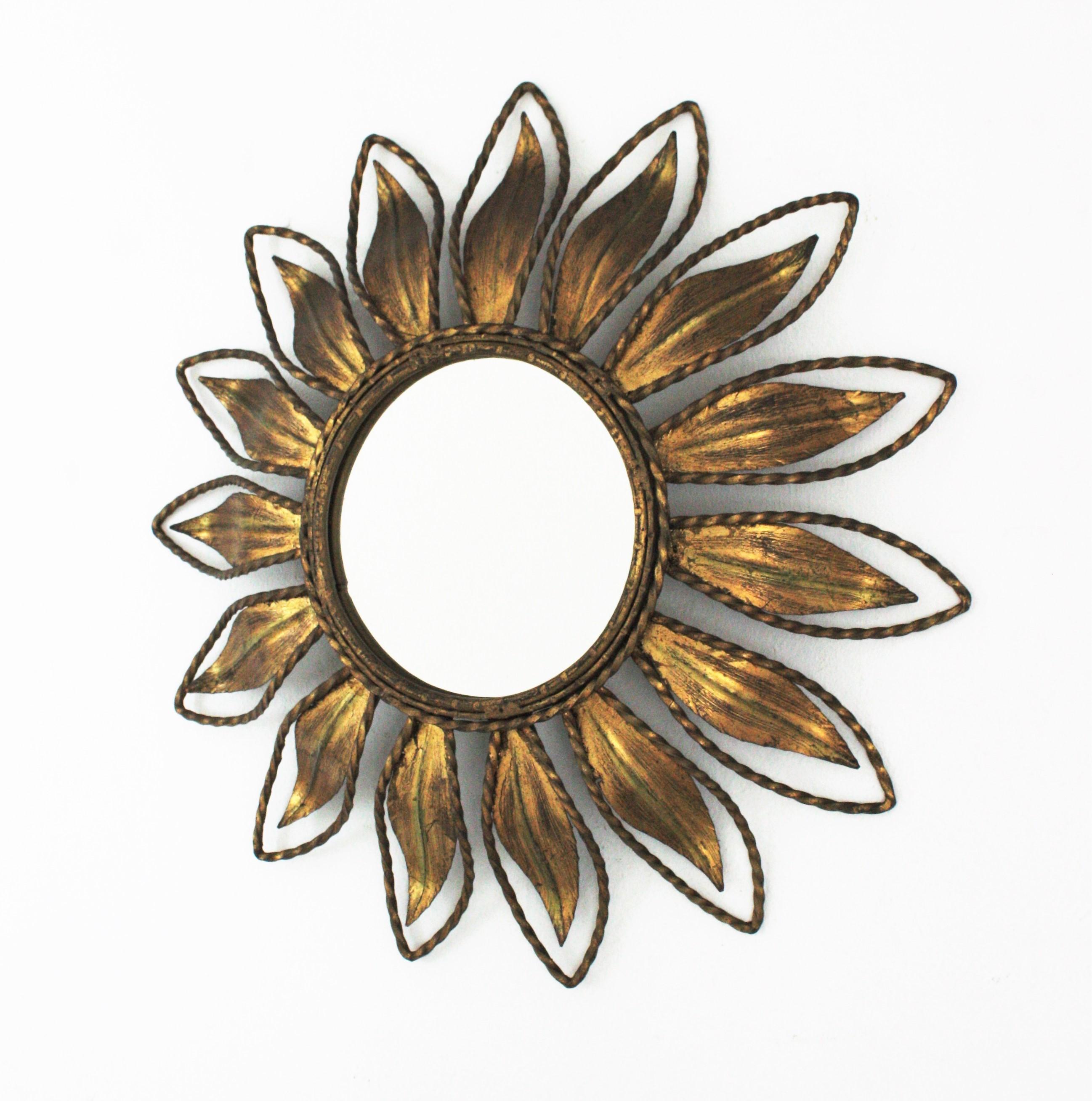 A beautiful gilt wrought iron leafed sunburst mirror with twisting iron rope detailings, Spain, 1960s.
This handcrafted wall mirror features a leafed frame surrounding a round glass. A twisted iron rope surrounds each leaf and the central glass. It