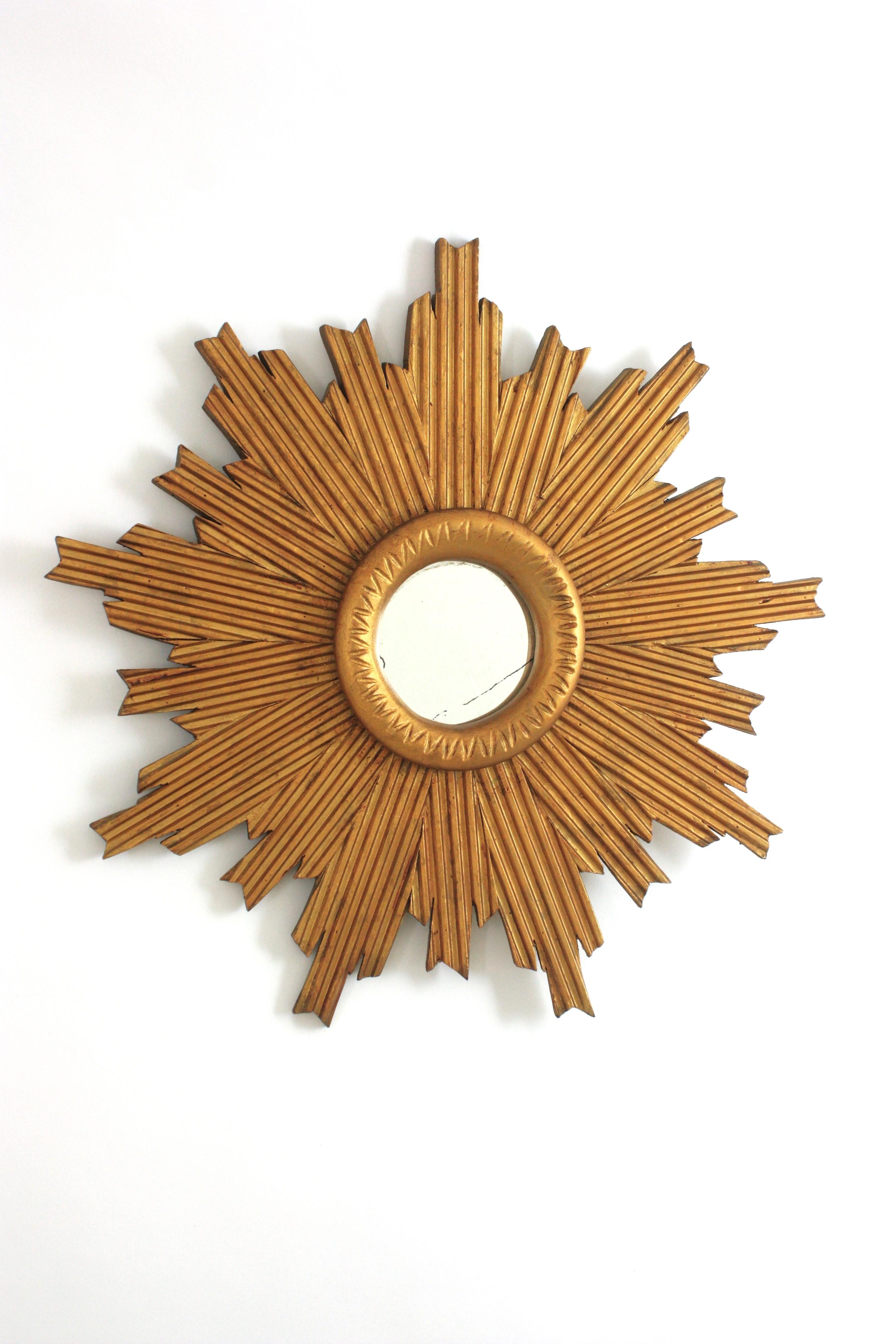 Mid-Century Modern Sunburst Mirror in gilt patinated carved wood with stripes. Spain, 1950s.
Eye-catching sunburst mirror with a design combining Midcentury and Brutalist accents. The frame is richly adorned by striped carved details and gilt