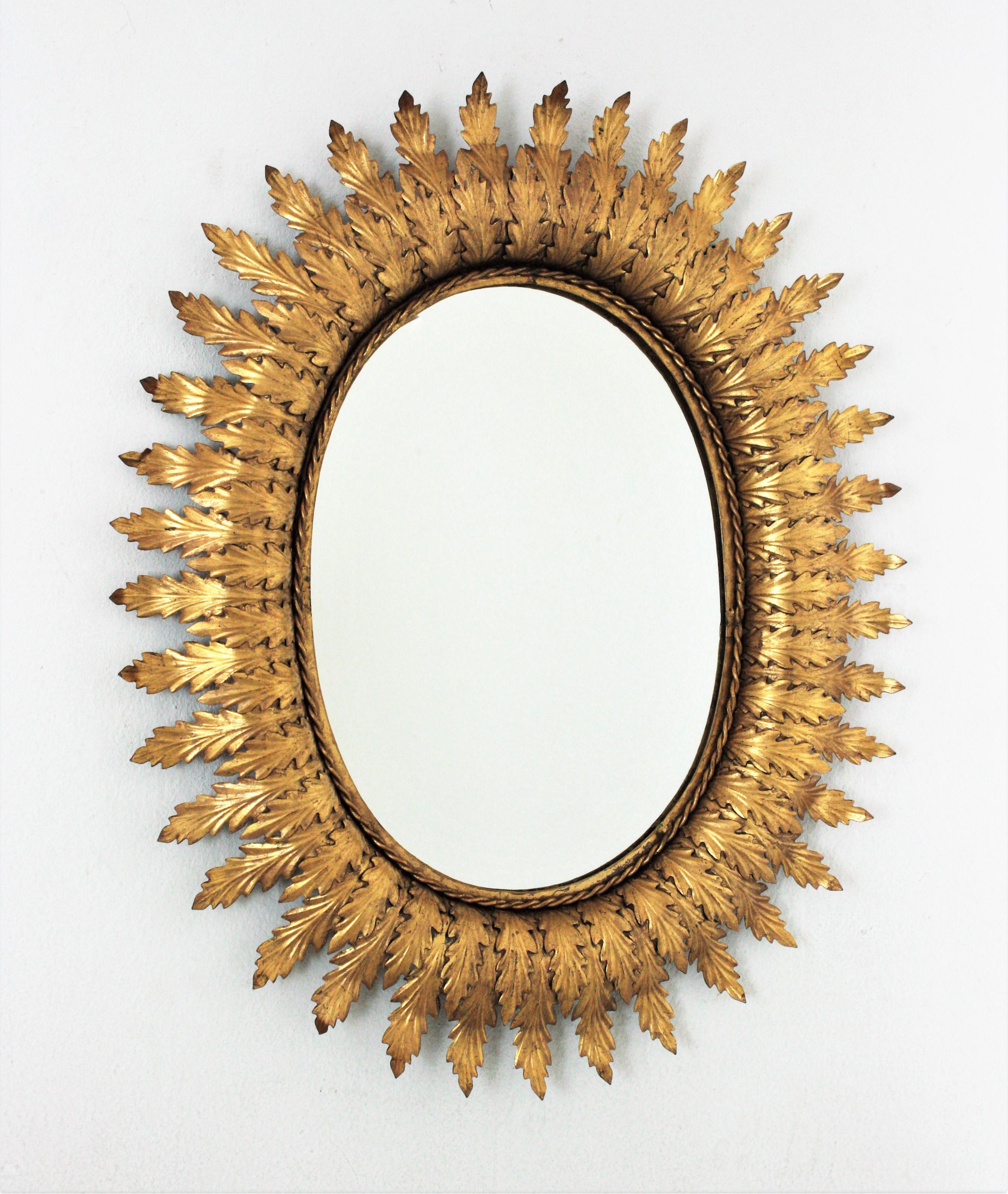 Eye-catching gilt metal oval shaped leafed sunburst mirror in the Hollywood Regency style, Spain, 1950s.
This beautiful wall mirror has a frame comprised of a series of overlaying leaves in two sizes. It has a nice aged patina and gold leaf