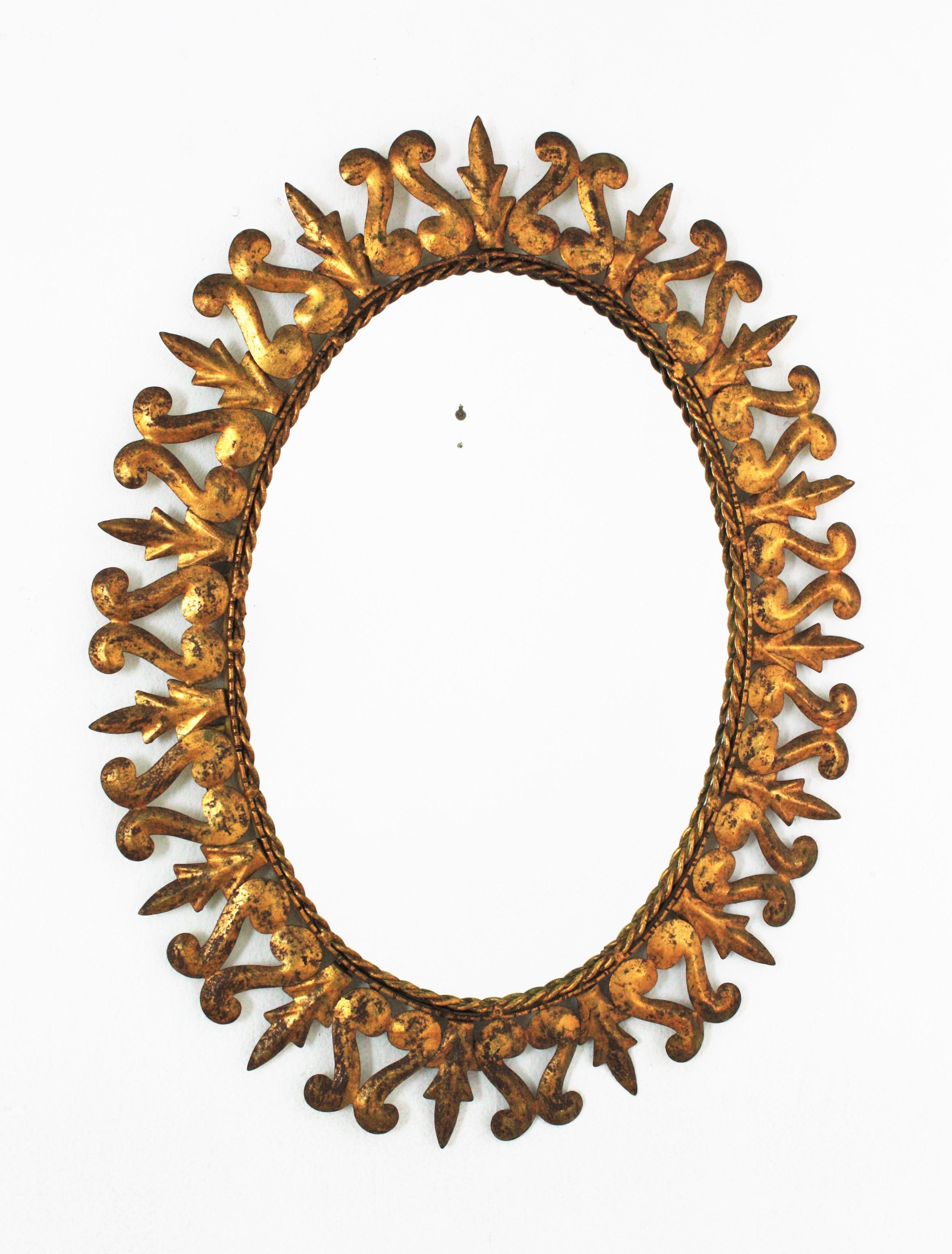 Oval sunburst mirror, Gilt iron, Gold Leaf,  Spain, 1950s
This hand-hammered iron sunburst wall mirror features a frame comprised by iron leaves alternating with scroll shaped details. It has a nice aged patina showing its original gold leaf gilding