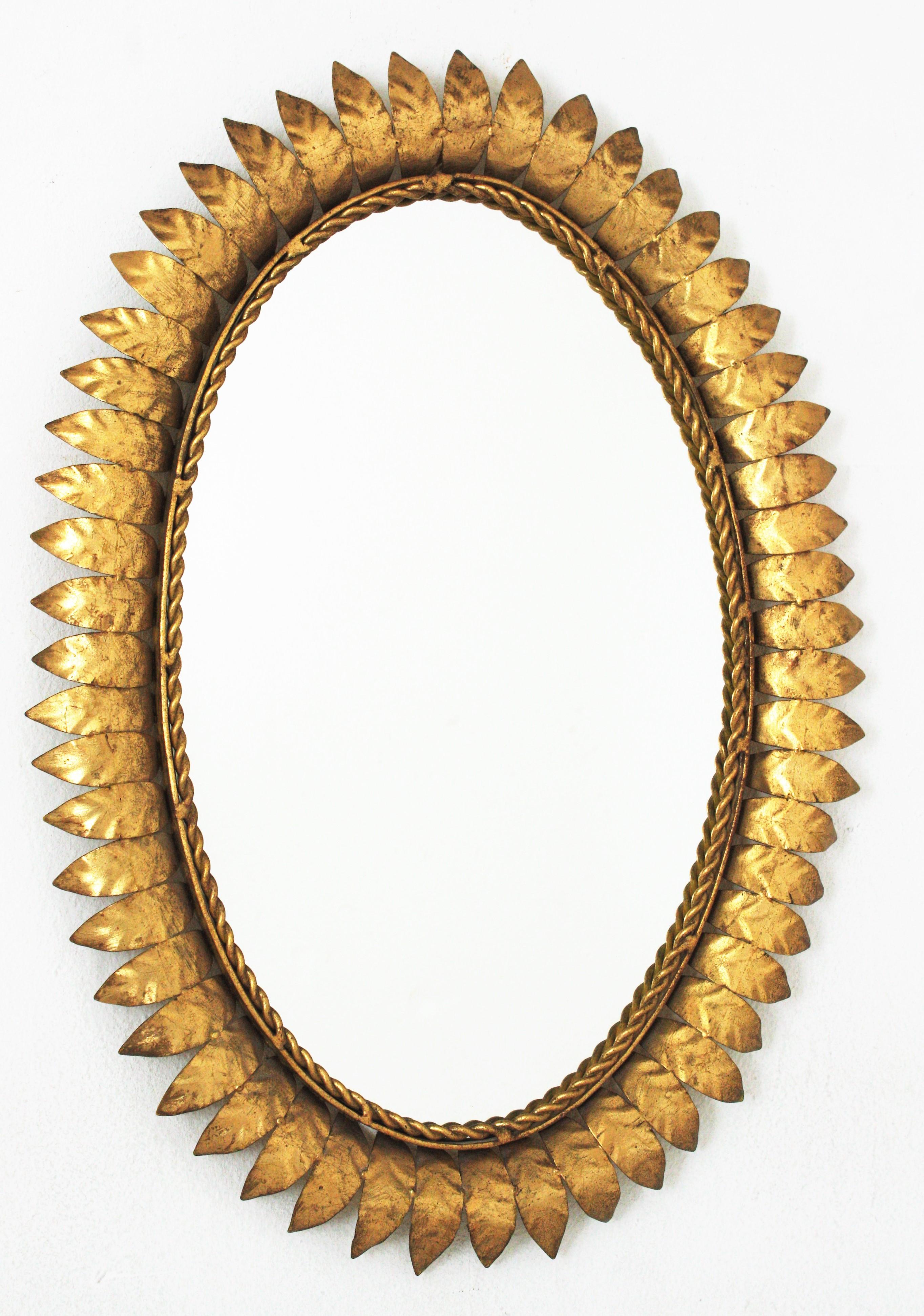 Mid-Century Modern iron sunburst oval wall mirror with leafed frame and gold leaf finish, Spain, 1950s.
This eye-catching leafed sunburst mirror has a very detailed frame, entirely made in gilt iron and showing its original patina and gold leaf
