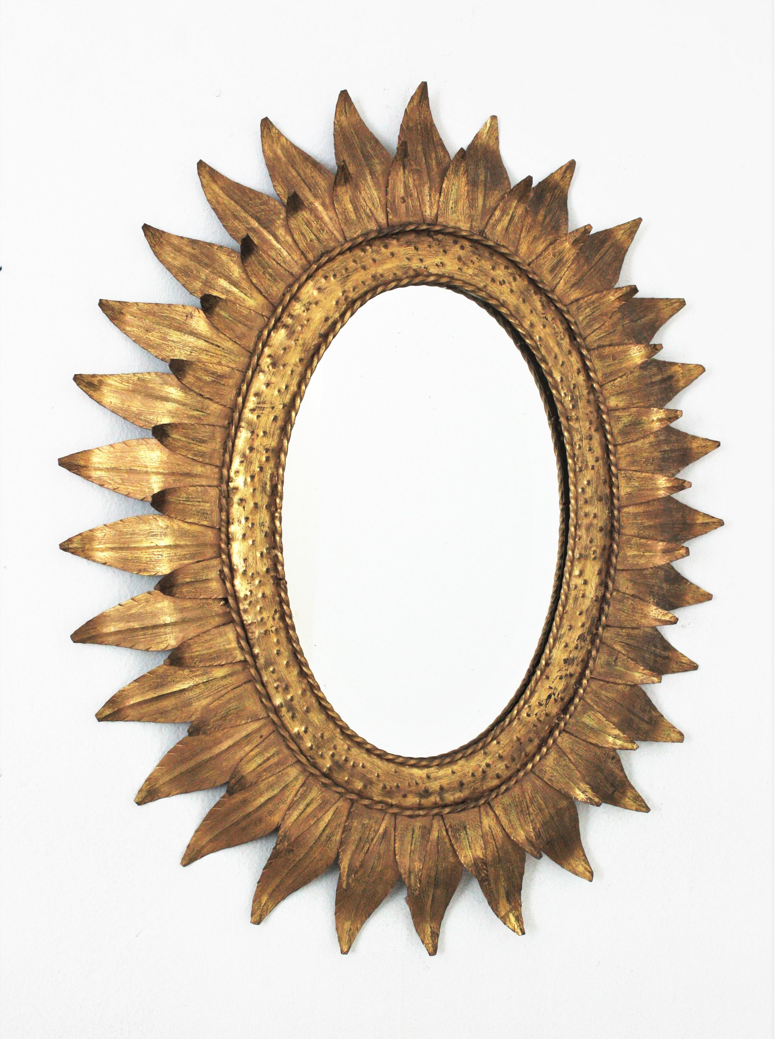 Oval sunburst mirror, Gilt iron. France, 1950s
This hand-hammered iron sunburst wall mirror features a double leafed oval frame heavily adorned by the hammer marks at the central part and twisting iron ropes surrounding the glass. It has a nice
