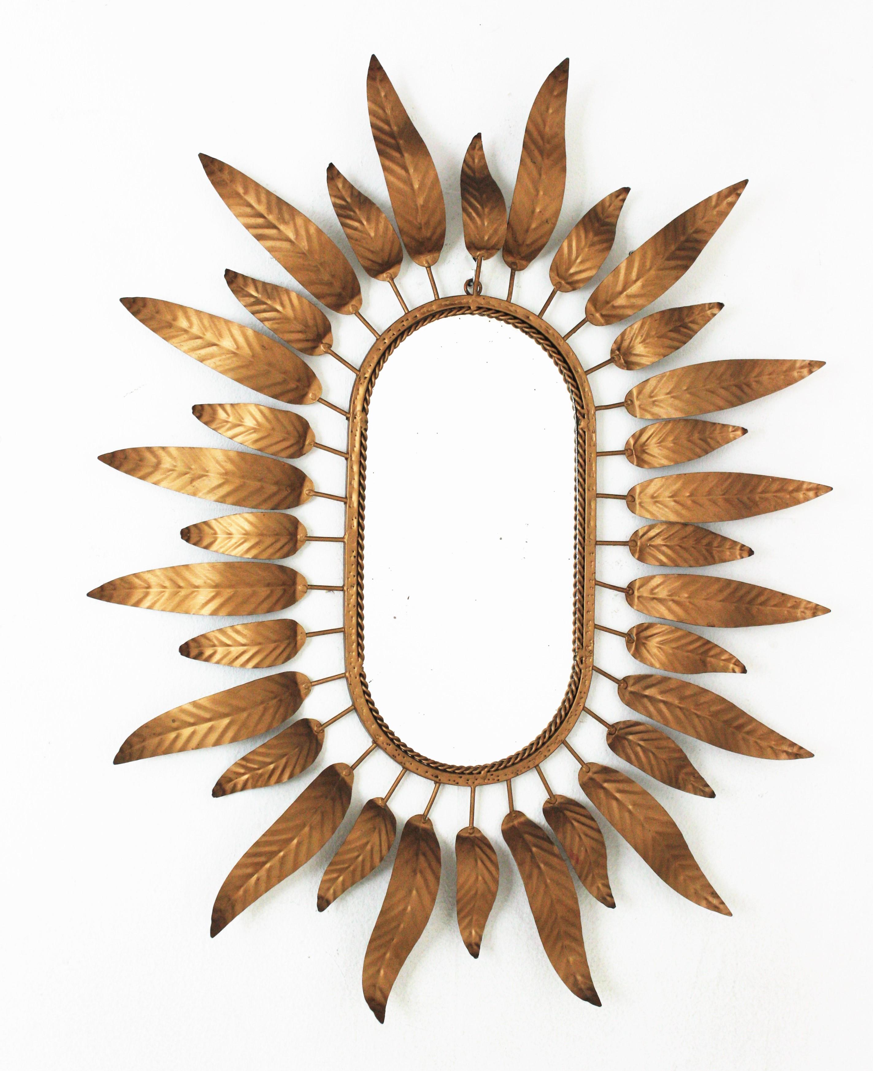 Gilt metal sunburst mirror framed by leaves. Spain, 1950s-1960s.

This stylish mirror combines Midcentury and Hollywood Regency accents.A highly decorative oval sunburst mirror with foliage frame. Elegant curved leaves in two sizes surrounding the