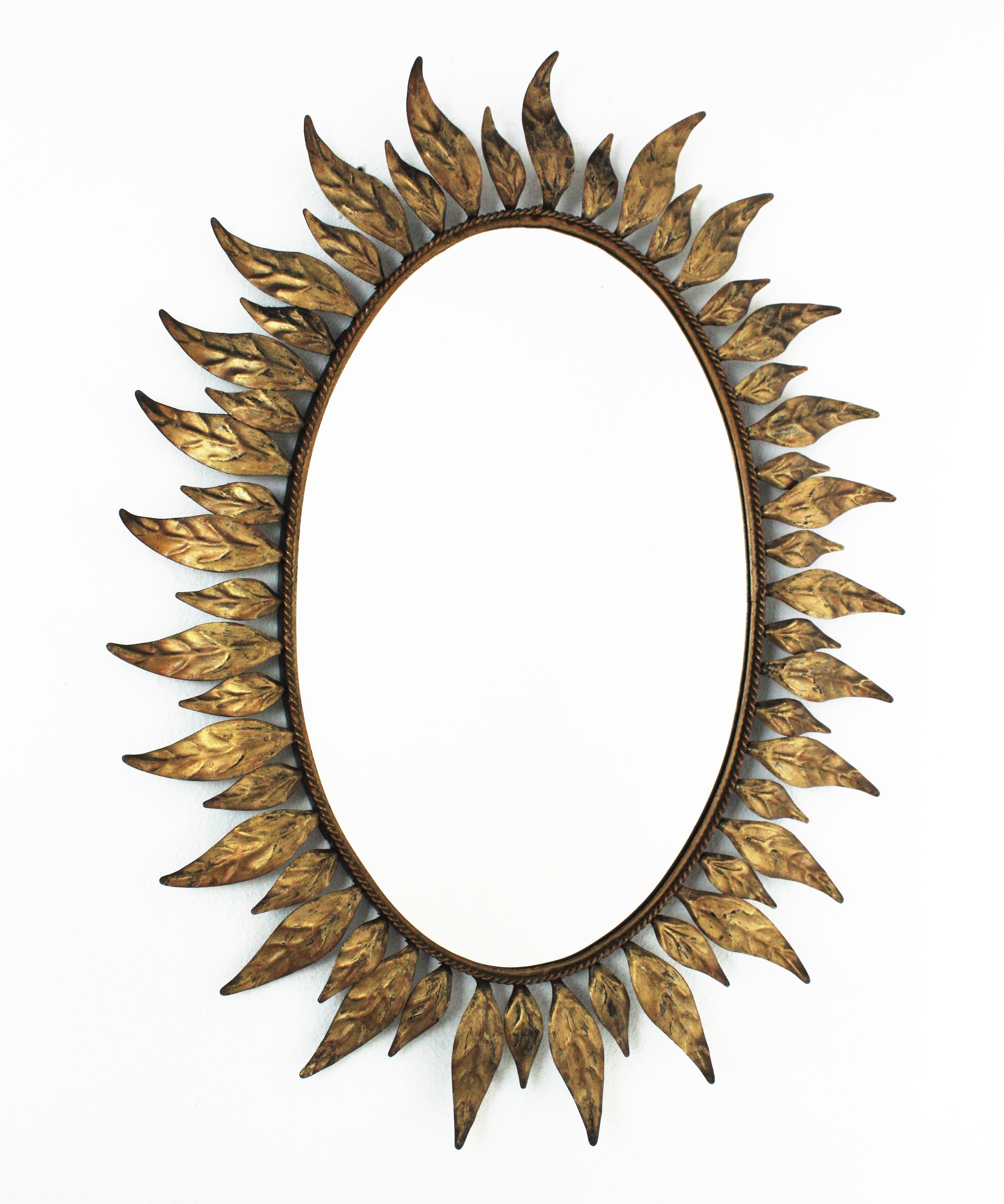 Gilt metal sunburst mirror framed with leaves in bronze, parcel-gilt color. Spain, 1950s-1960s.
A highly decorative oval sunburst mirror framed with elegant curved leaves in two sizes.
This mirror is in excellent vintage condition and has a