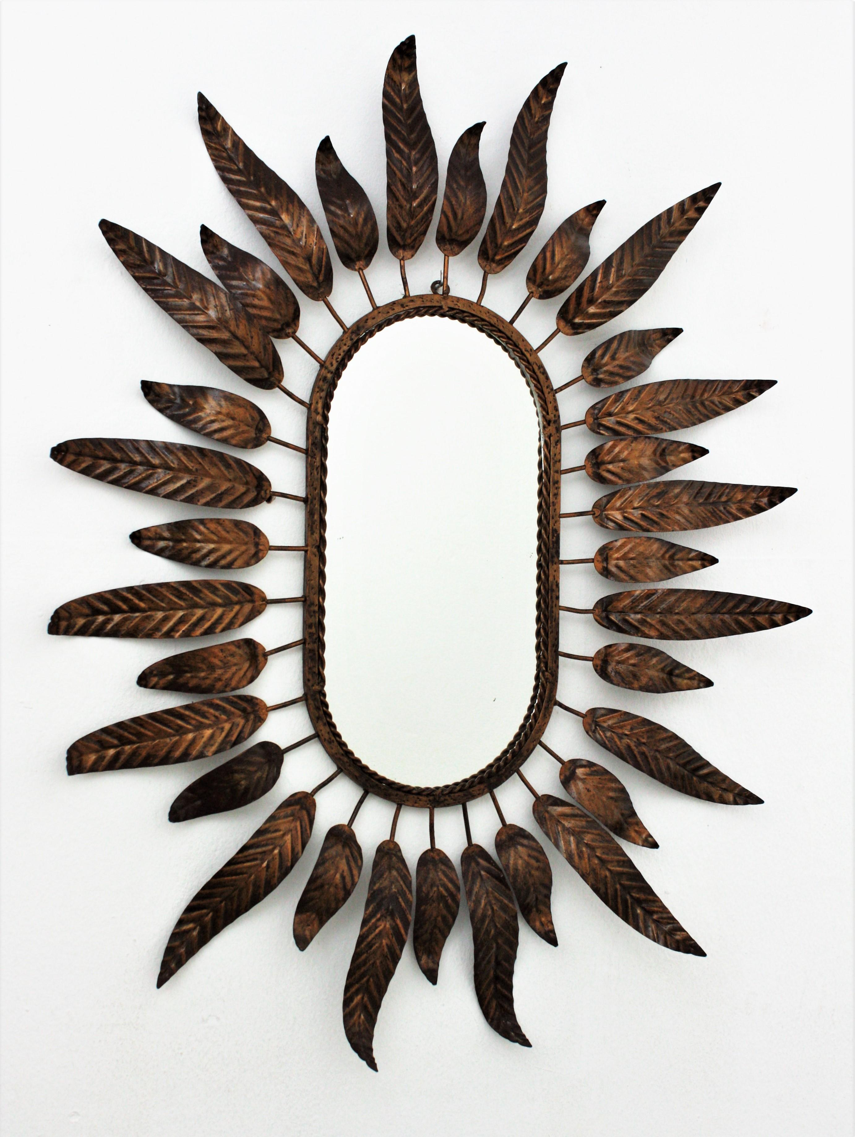 Gilt metal sunburst mirror framed with leaves in bronze, parcel-gilt color. Spain, 1950s-1960s.
A highly decorative oval sunburst or flower burst mirror framed with elegant curved leaves in two sizes.
This mirror is in excellent vintage condition