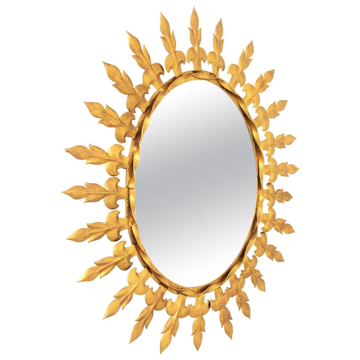 Sunburst Oval Wall Mirror with Fleur de Lys Frame in Gilt Iron, Spain, 1950s
Mid- century Modern Sunburst Mirror in Gilt Metal. 
The frame is comprised by alternating leaves or Fleur de Lys motifs joined between them by a twisted strip. 
This wall