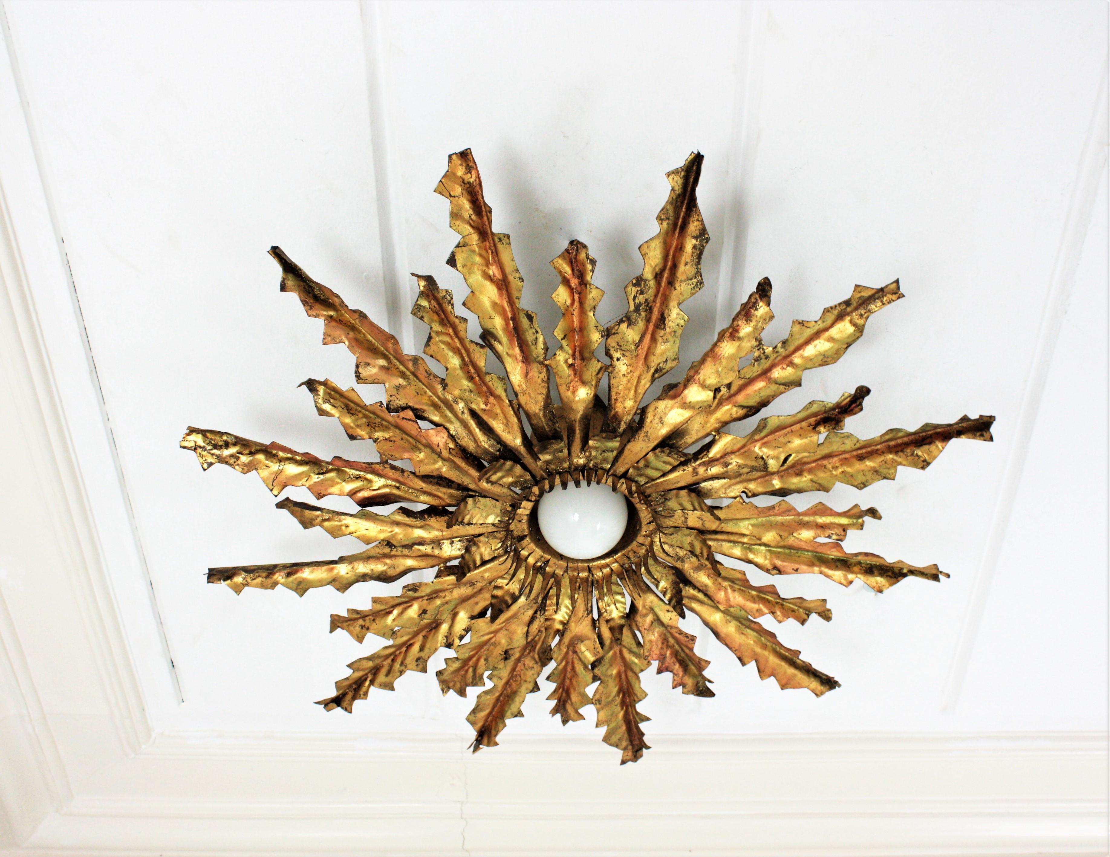 Monumental brutalist sunburst starburst leafed gilt metal pendant lamp or ceiling light fixture. Spain, 1950s
This handcrafted Brutalist ceiling lamp features a triple layered leafed sunburst light fixture hanging from a chain ended with a beautiful