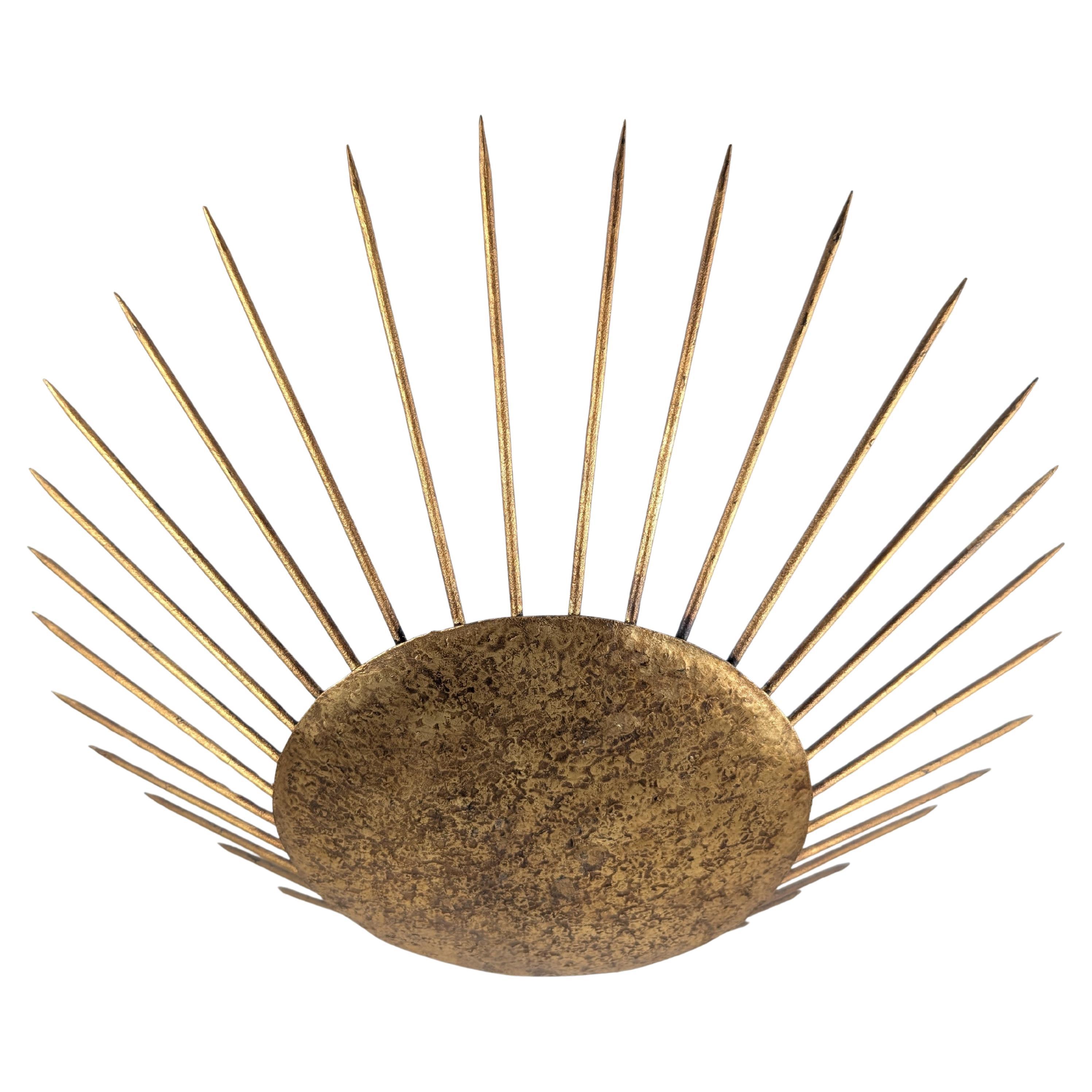 Elegant sunburst pendant lamp crafted in hammered gilt metal, offering a striking reinterpretation of the neoclassical solar motif through the lens of mid-century French design. A circular hammered center radiates dynamic rays in perfect symmetry,