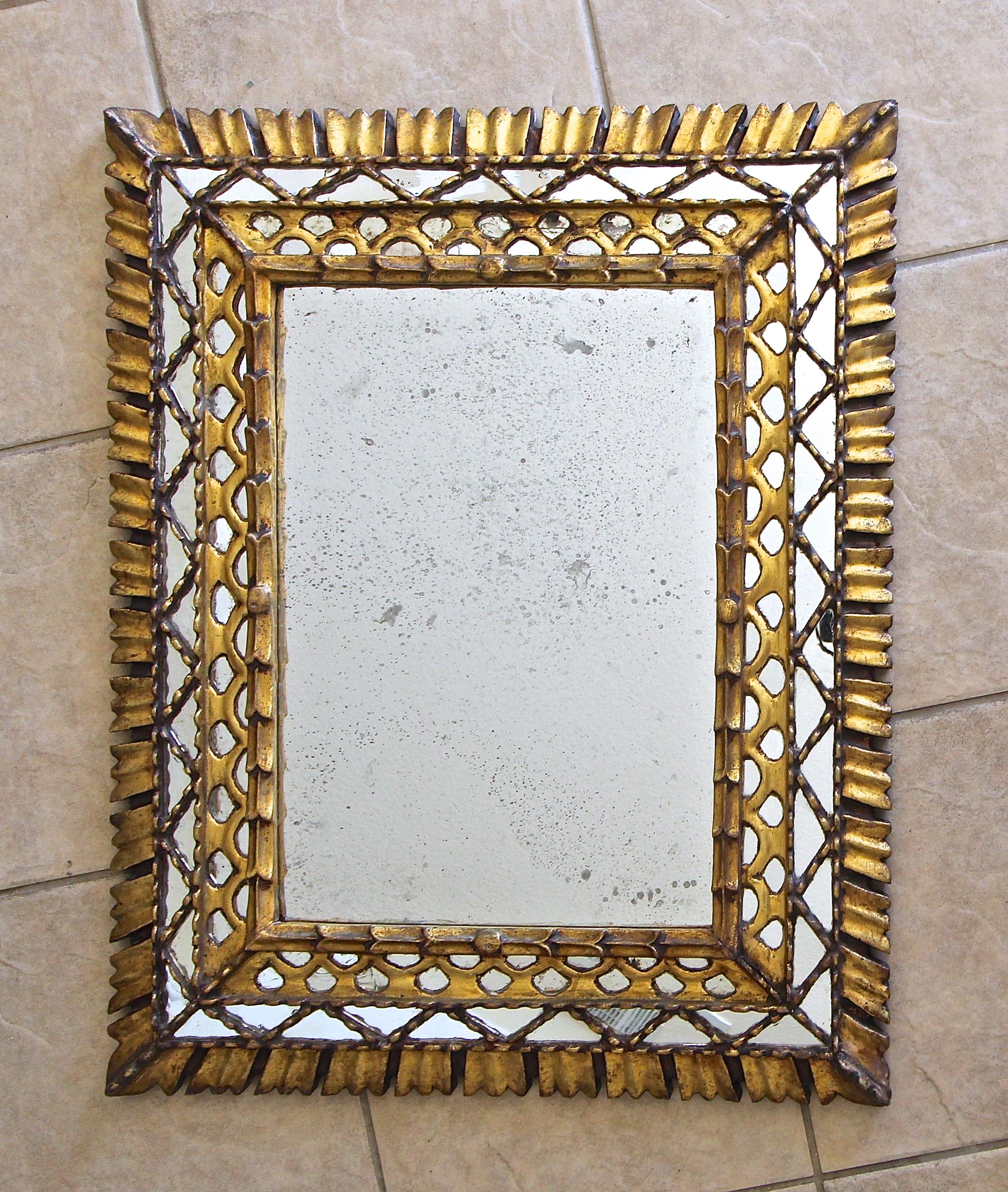 Hand carved rectangle shaped colonial Spanish wall mirror in gold giltwood and gesso finish. There are 3 interior rows of smaller inset mirrors, with carved giltwood outer rays. The larger center mirror is 19