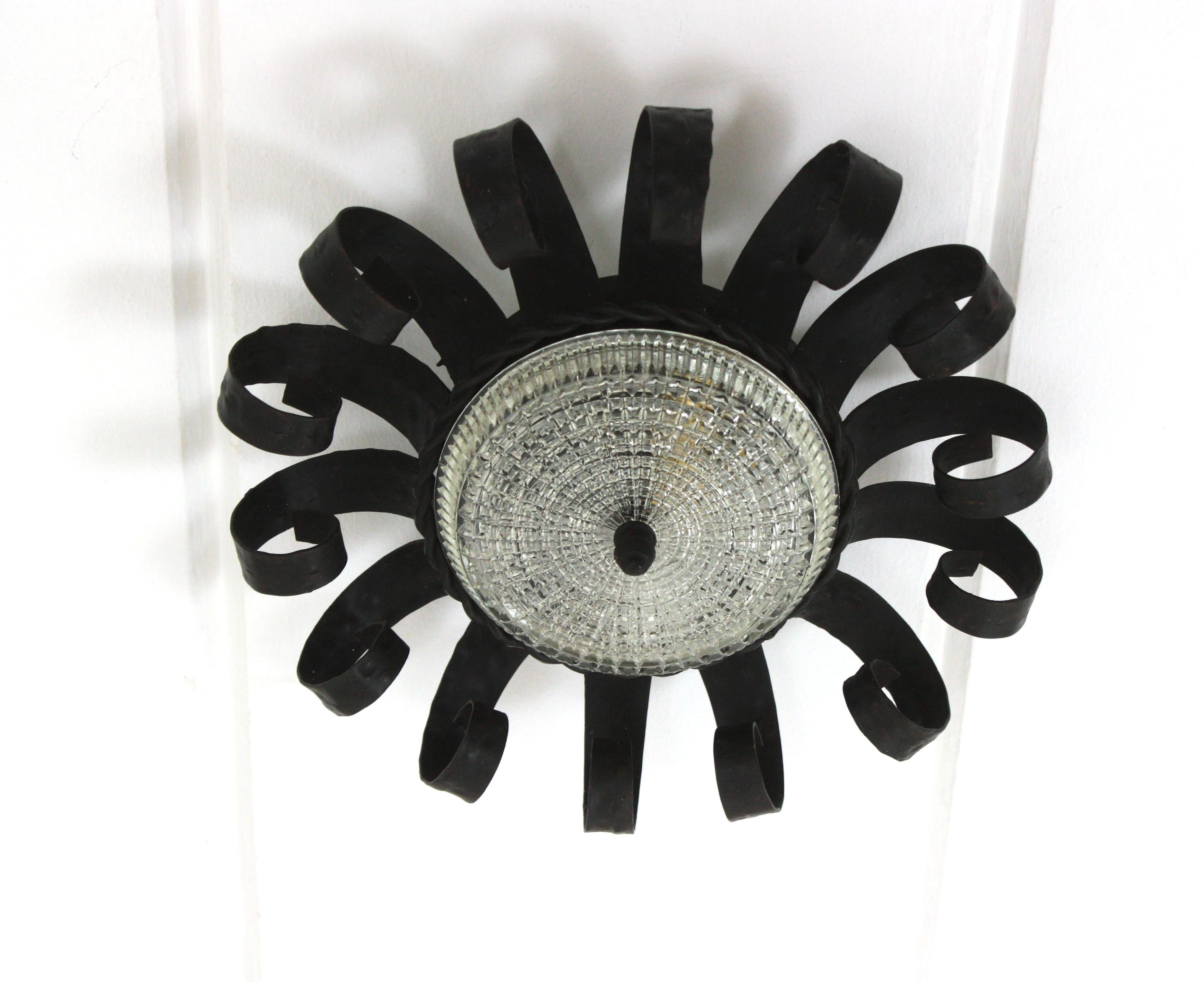 Brutaliste forgé à la main  Luminaire en fer avec abat-jour en verre pressé, Espagne, années 1950
Ce luminaire en forme de couronne de soleil, fabriqué à la main, est doté d'un cadre en fer forgé et d'un difuseur central en verre pressé.
Le travail