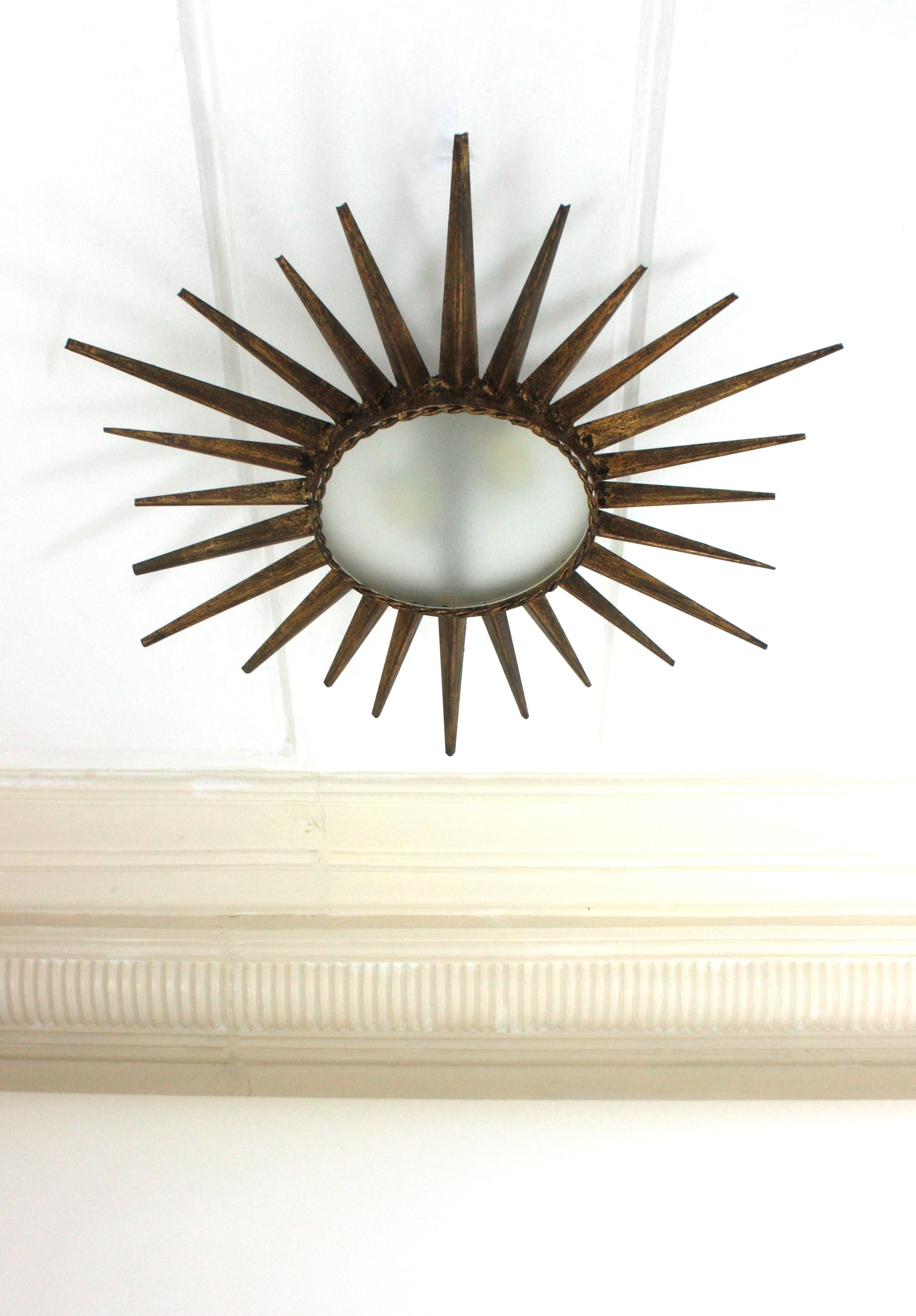Luminaire brutaliste en fer doré, France, années 1950.
A la manière de Gilbert Poillerat.
Monture encastrée en fer martelé à la main avec abat-jour en verre dépoli. Il présente une alternance de rayons longs et courts autour d'un diffuseur central