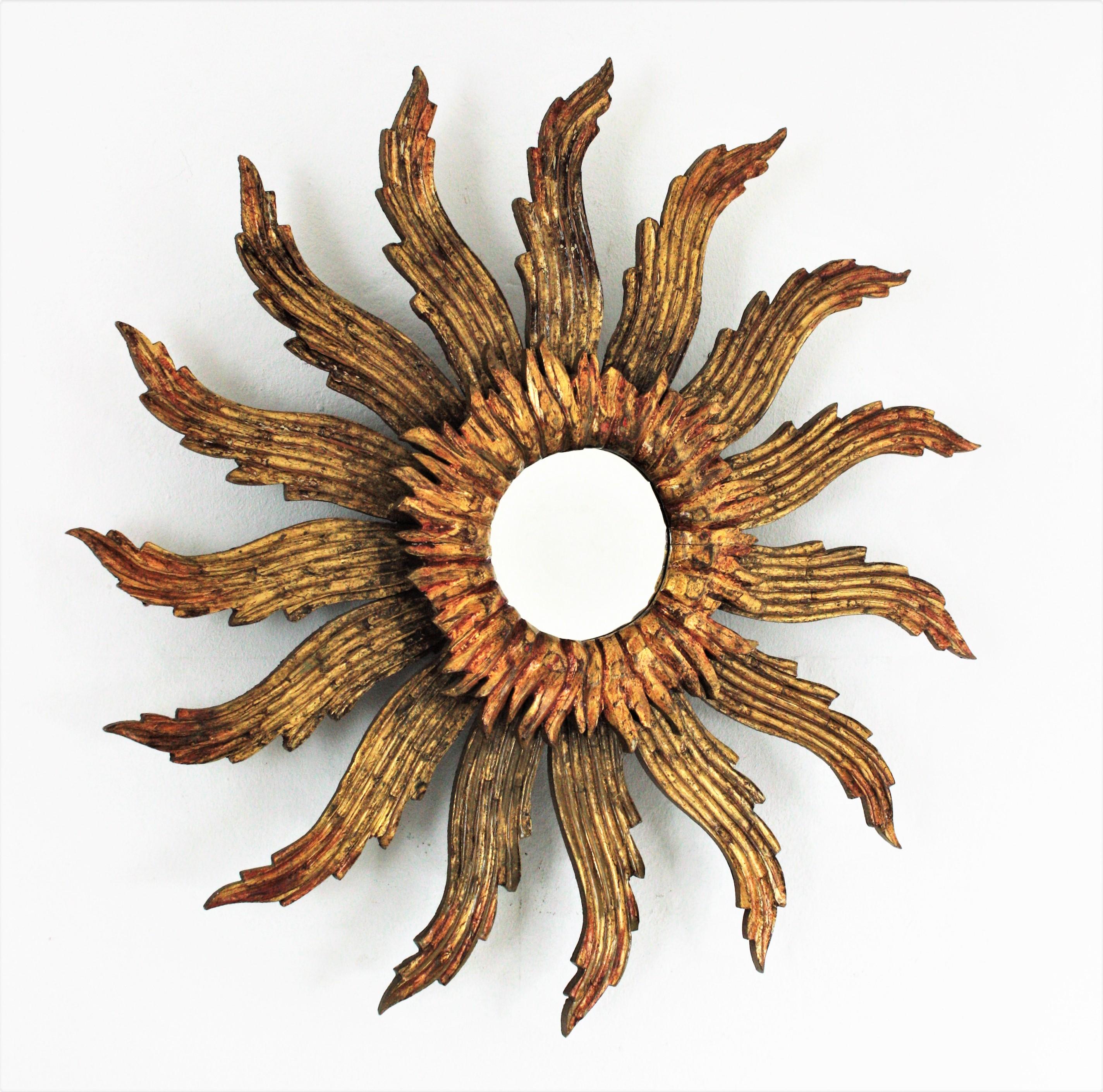 Large Baroque style carved giltwood sunburst mirror. France, 1950s
Eye-catching giltwood sunburst mirror with large rays in pinwheel disposition and small beams surrounding the central glass.
This wall mirror has richly carved details and gold