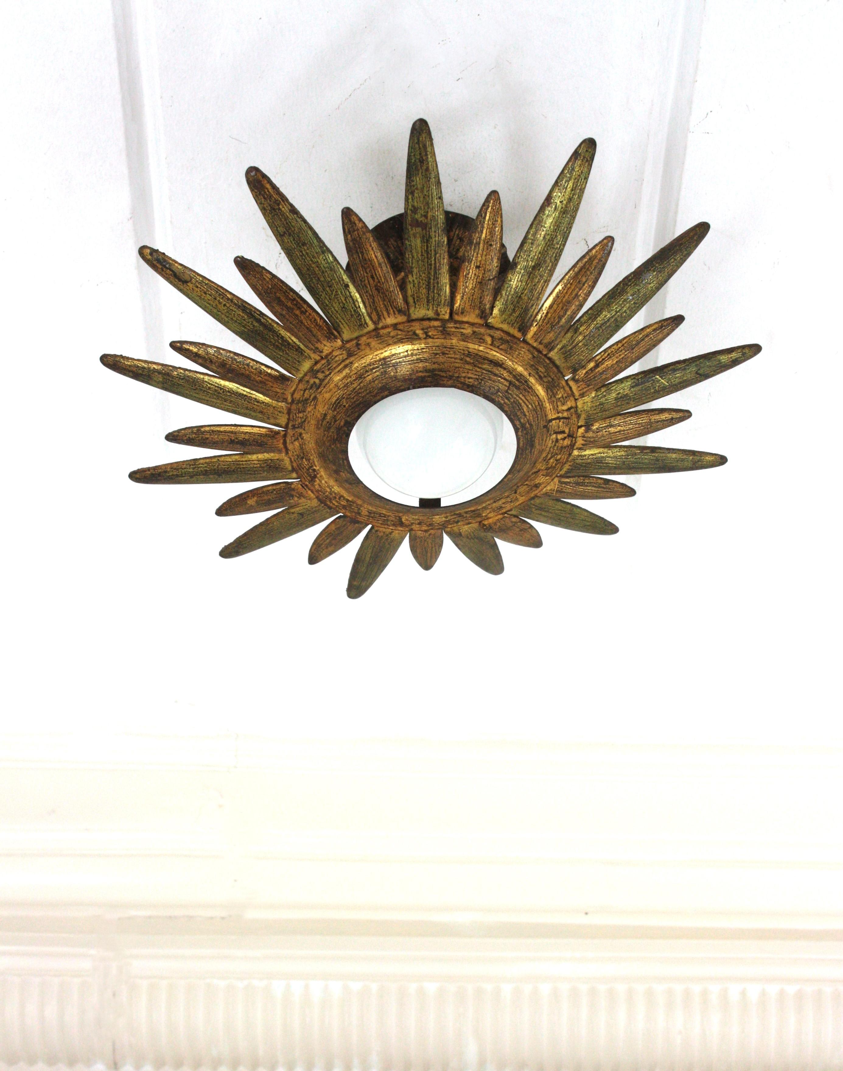 Eye-catching gilt wrought iron sunburst or starburst shaped ceiling light fixture or pendant, Spain, 1960s.
The starburst / sunburst shaped frame surrounds a central exposed bulb. 
This flush mount has a terrific aged patina and shows its original