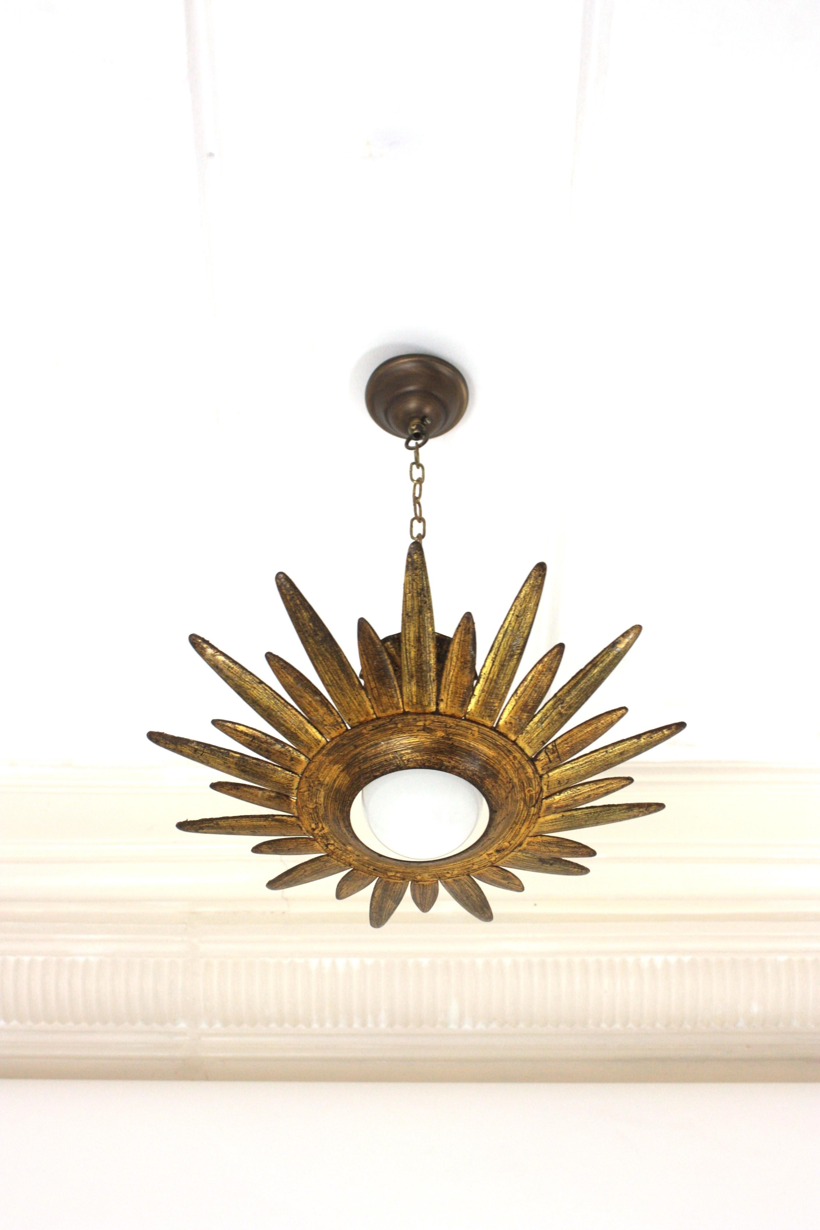 Eye-catching gilt wrought iron sunburst or starburst shaped ceiling light fixture or pendant, Spain, 1960s.
The starburst / sunburst shaped frame surrounds a central exposed bulb. 
This flush mount has a terrific aged patina and shows its original
