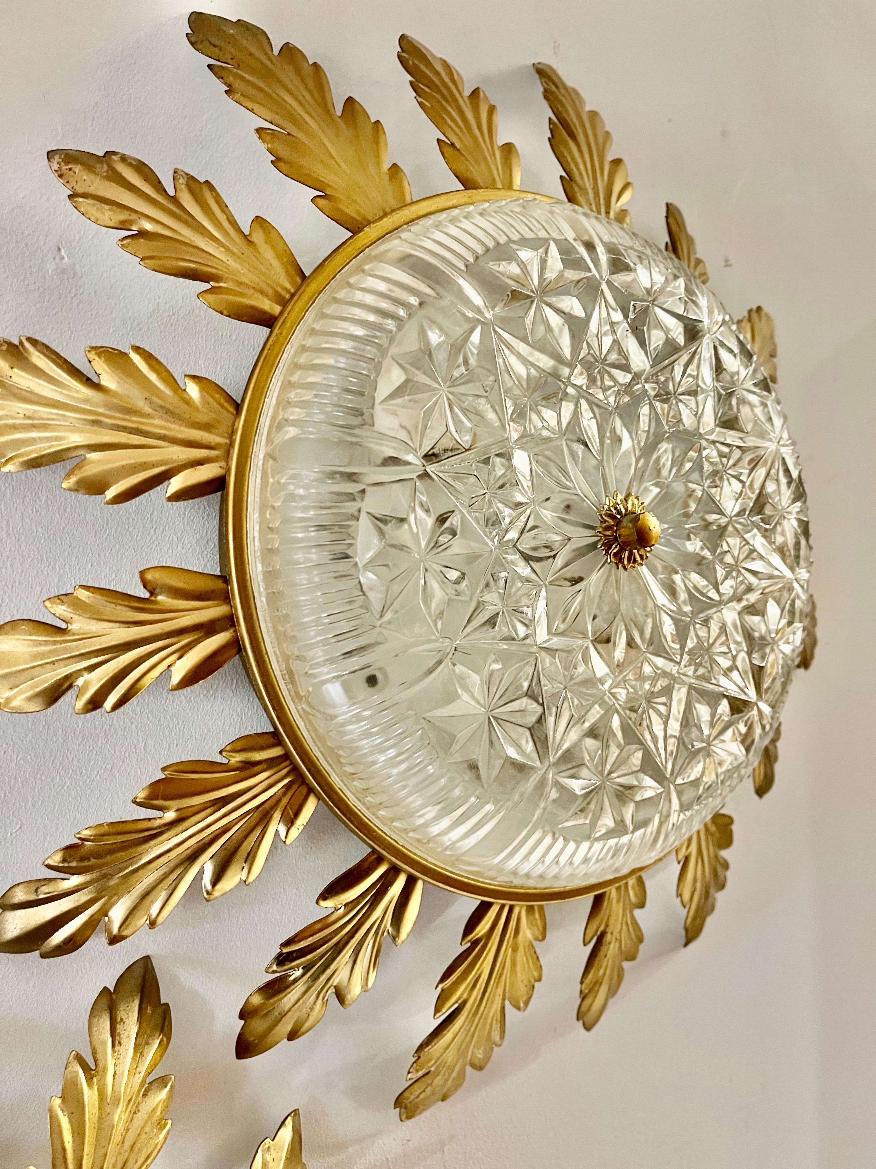 Iconic sunburst lamp in guilt gold metal with two E27 lights in the center. Handcrafted and hammered iron finished in gold leaf with a nicely aged patina. with crystal glass

This functionality can be used as recessed mounting or as a wall element.