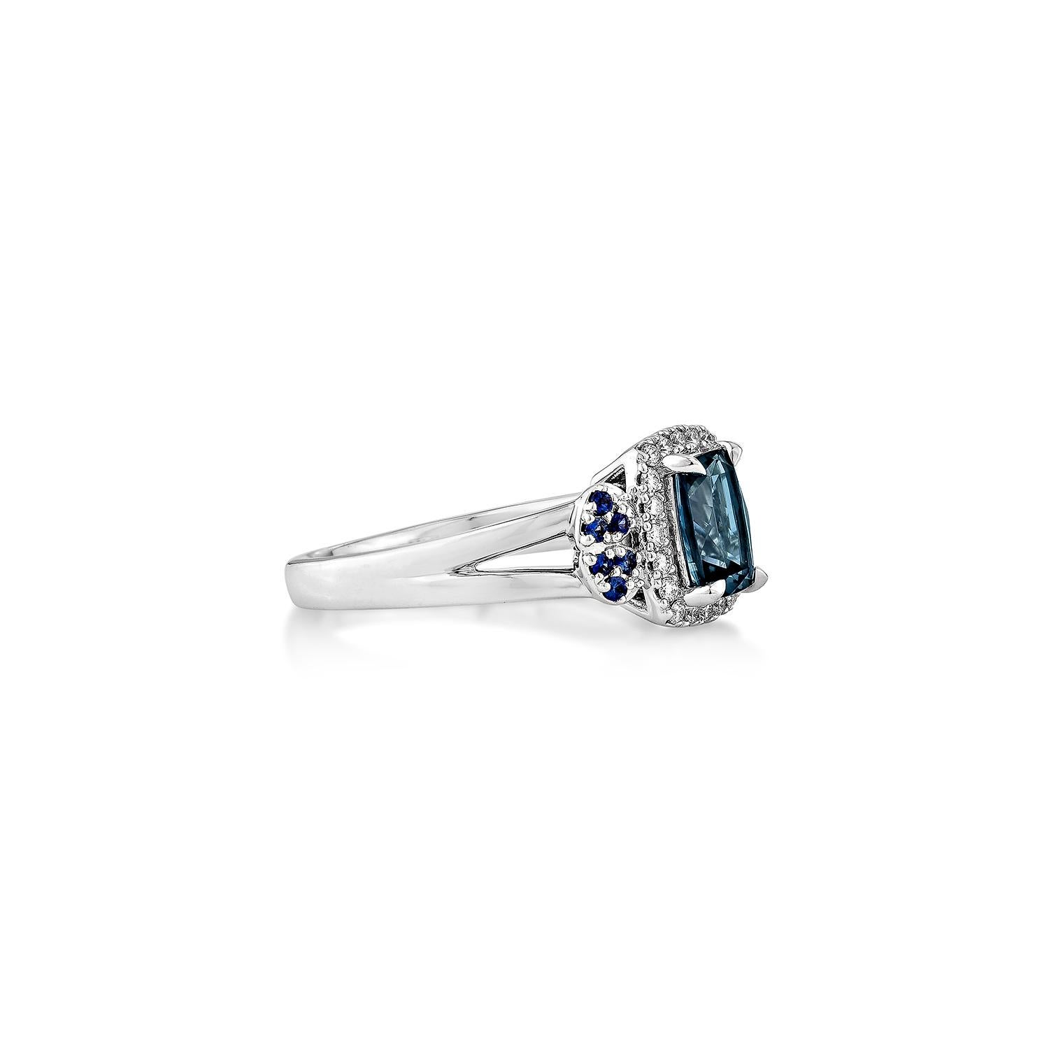 Dieser fesselnde, ausgefallene Ring zeigt einen auffälligen Londoner Blautopas im Kissenschliff, der in 14 Karat Weißgold gefasst ist und tiefe ozeanische Farbtöne ausstrahlt. Eingerahmt von einem Halo aus weißen Brillanten und ergänzt durch