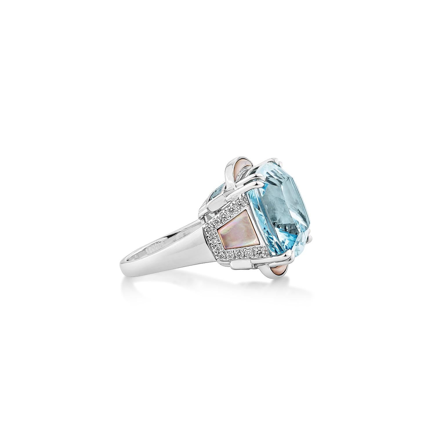 This striking statement ring features a stunning cushion-cut aquamarine, radiating exceptional brilliance and clarity. The center stone is beautifully complemented by inlaid pink mother of pearl accents on the sides, adding an elegant iridescent