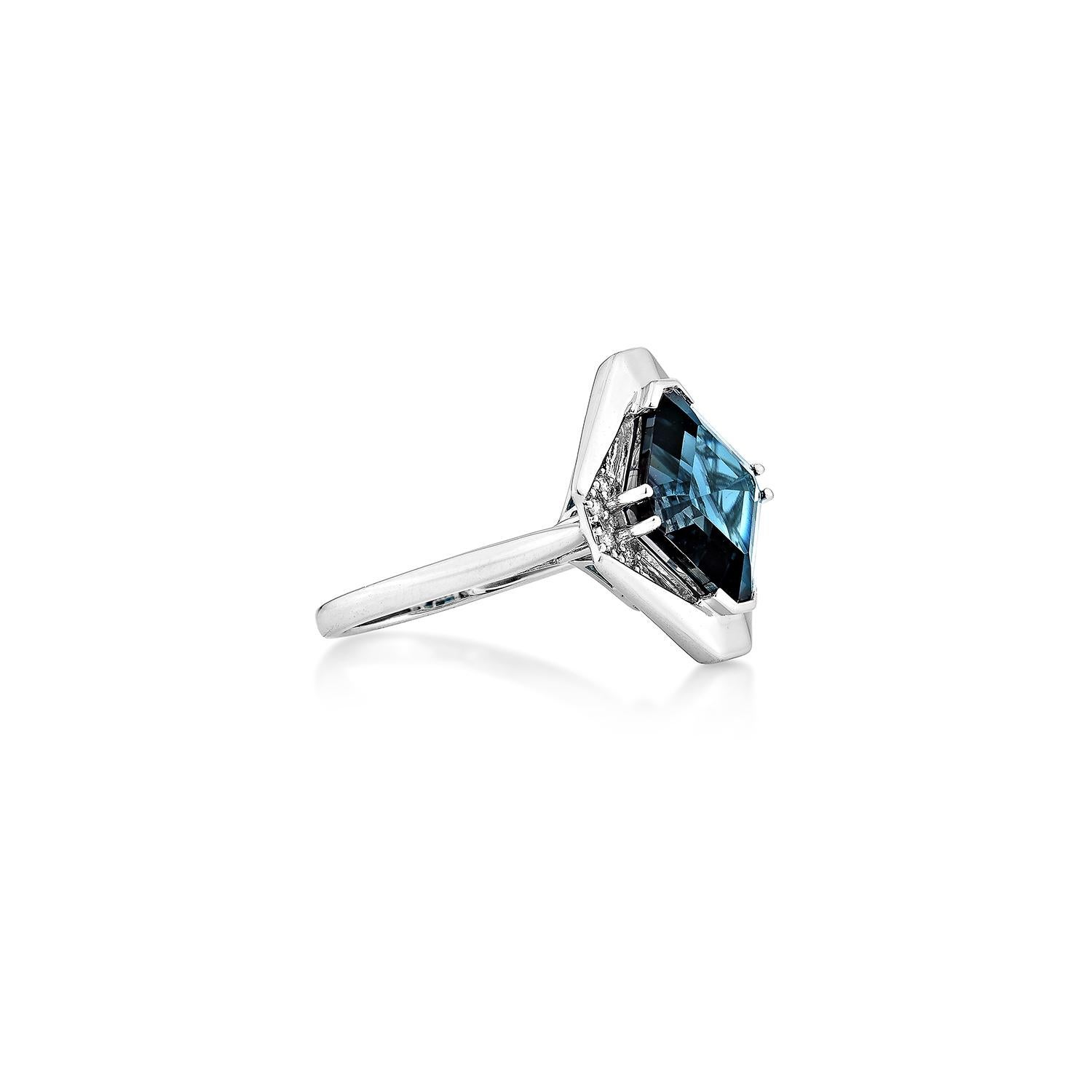 Este elegante anillo, una audaz declaración geométrica, presenta un topacio azul de Londres ricamente saturado en talla fantasía, enmarcado por brillantes diamantes blancos. Engastado en oro blanco pulido de 14 quilates, su moderno diseño angular